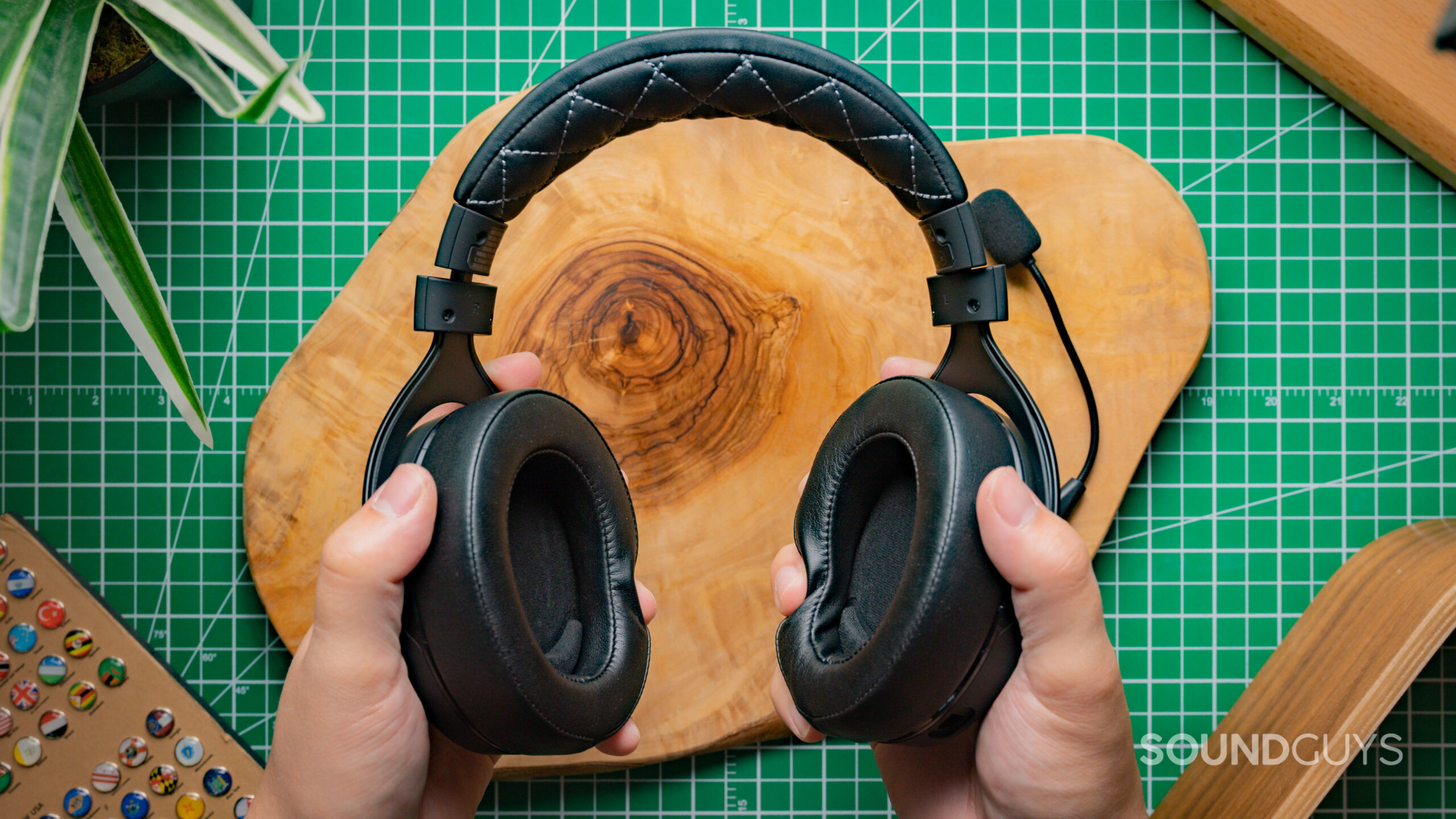 The Corsair HS70 Pro Wireless being held in two hands against a wood backdrop on top of a green table.