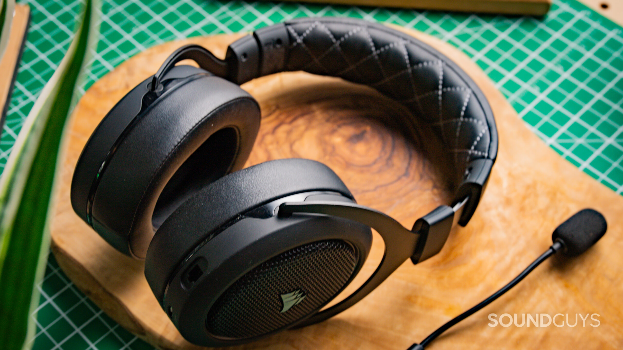 The Corsair HS70 Pro Wireless sitting on a wooden surface at a side angle, with the detachable microphone next to it.