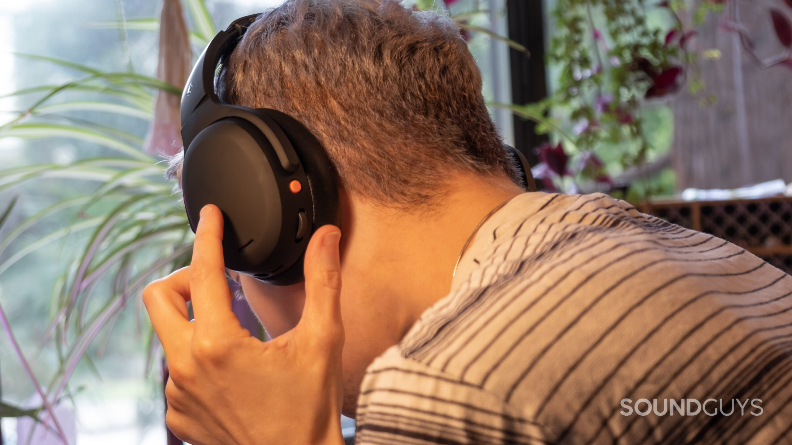 A man faces away from the camera wearing the Skullcandy Crusher ANC 2 about to operate the Crusher dial in front of a window.