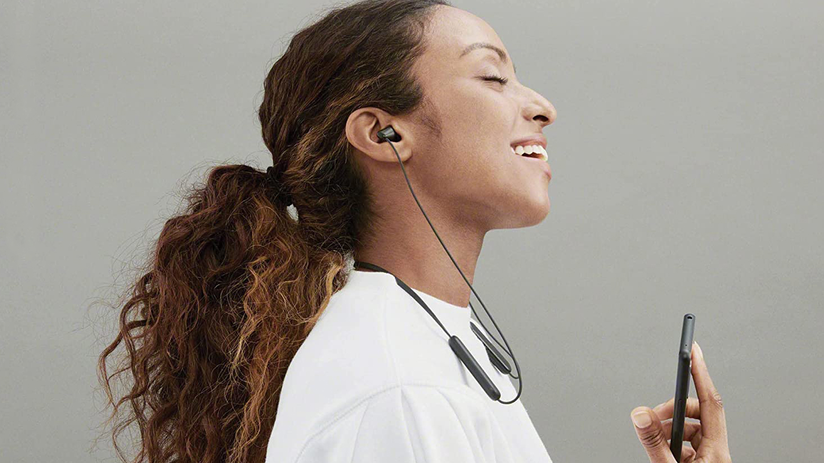 A woman smiles wearing the Sony WI-C100 while facing right.