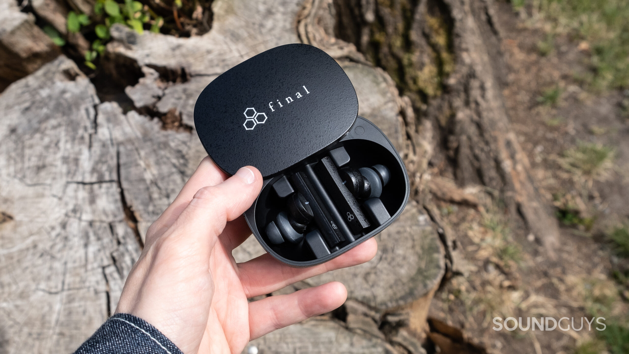 A hand holds the open case of the Final ZE8000 in front of a tree stump.