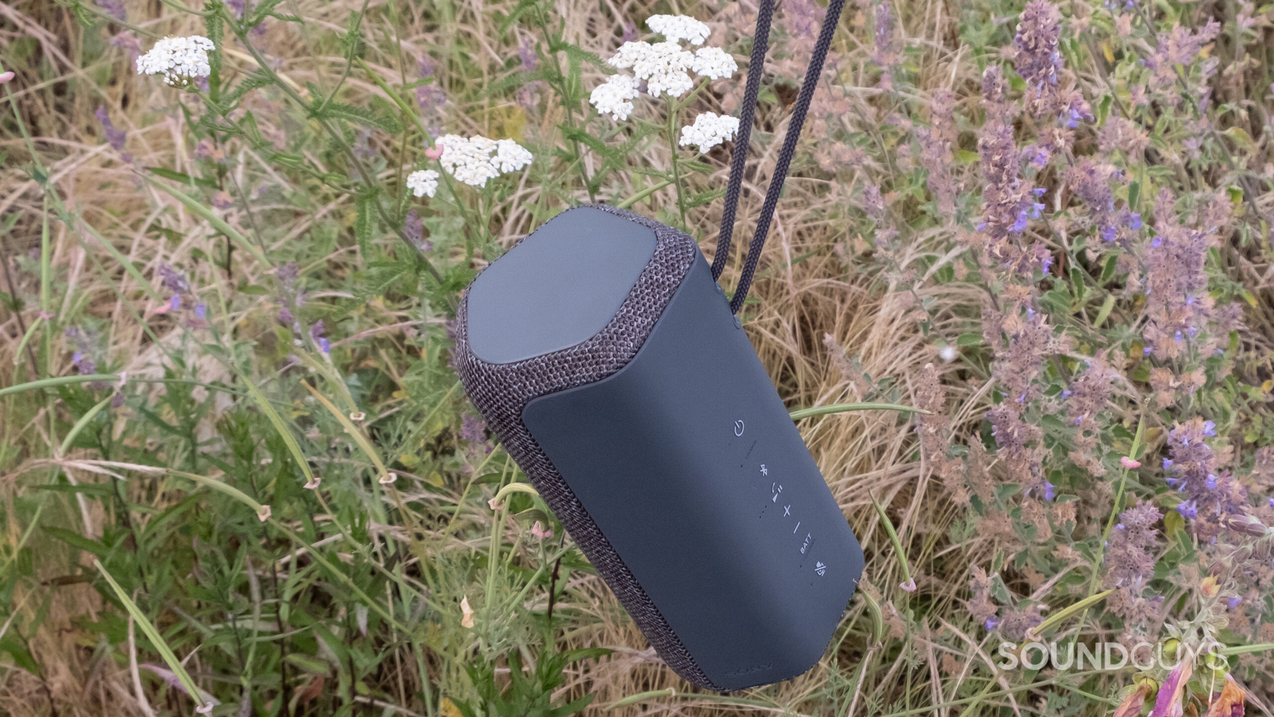 The Sony SRS-XE200 dangles by its cord in front of a wild garden