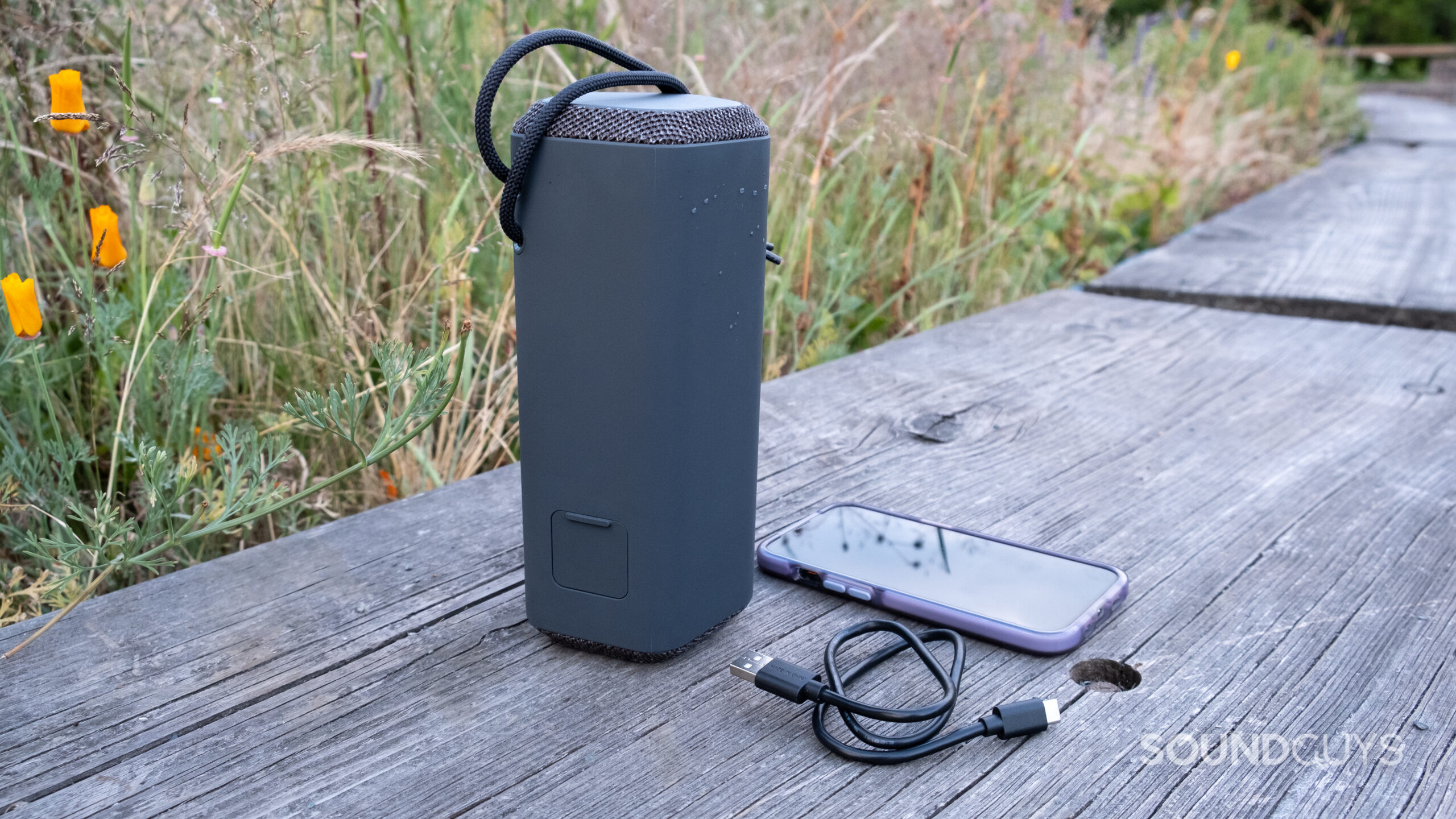 The Sony SRS-XE200 with its cable next to an iPhone on a wood surface.