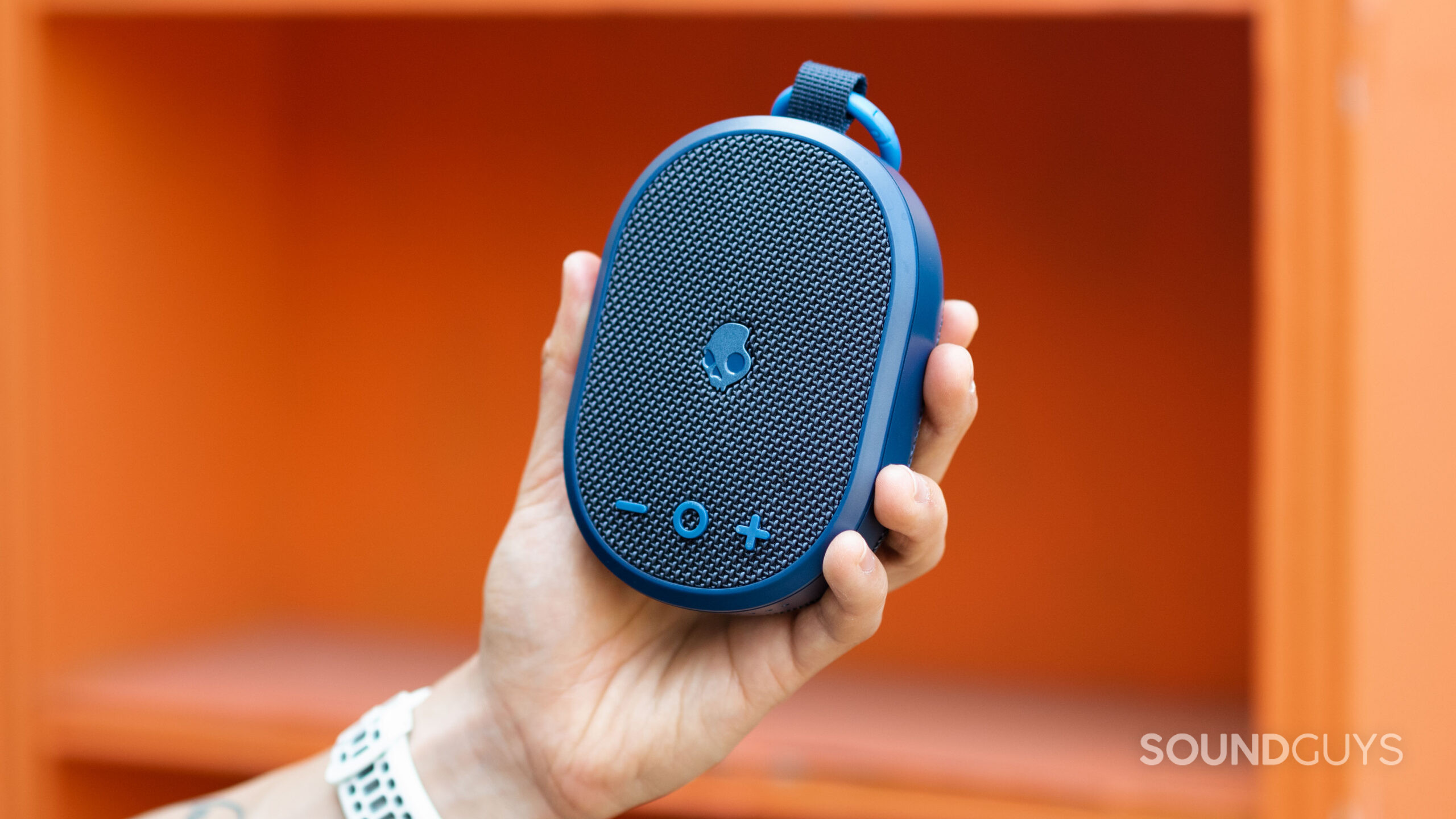 A hand holds the Skullcandy Kilo Bluetooth speaker against an orange background.