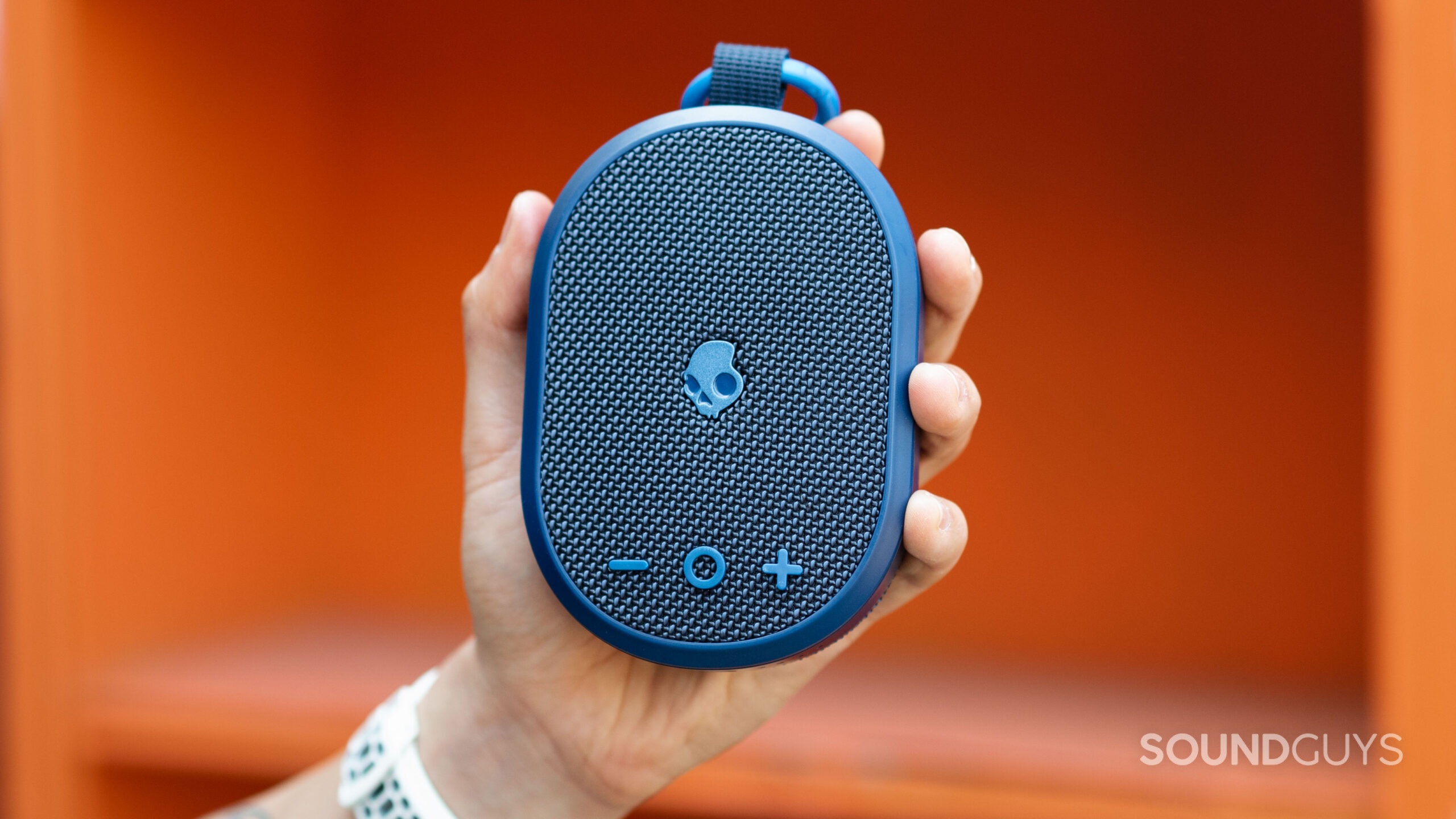 A hand holds the Skullcandy Kilo Bluetooth speaker against an orange background.