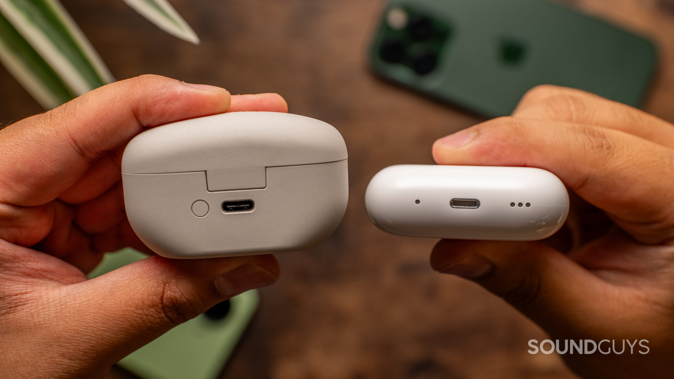 Hands hold the Sony WF-1000XM5 and Apple AirPods Pro (2nd generation) charging cases with their ports in view.