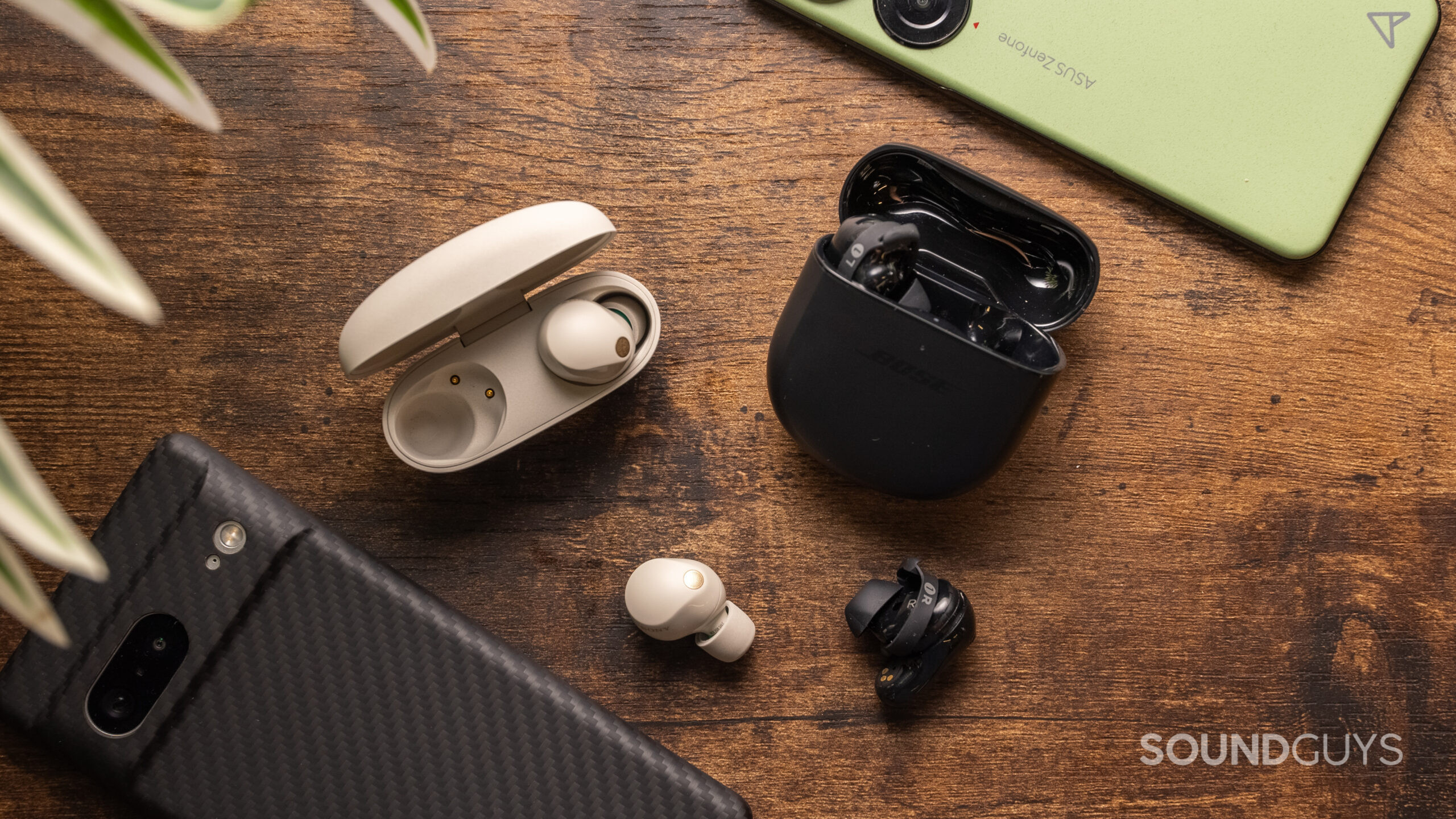 The Sony WF-1000XM5 and the Bose QuietComfort Earbuds II sitting side by side on a wooden table.