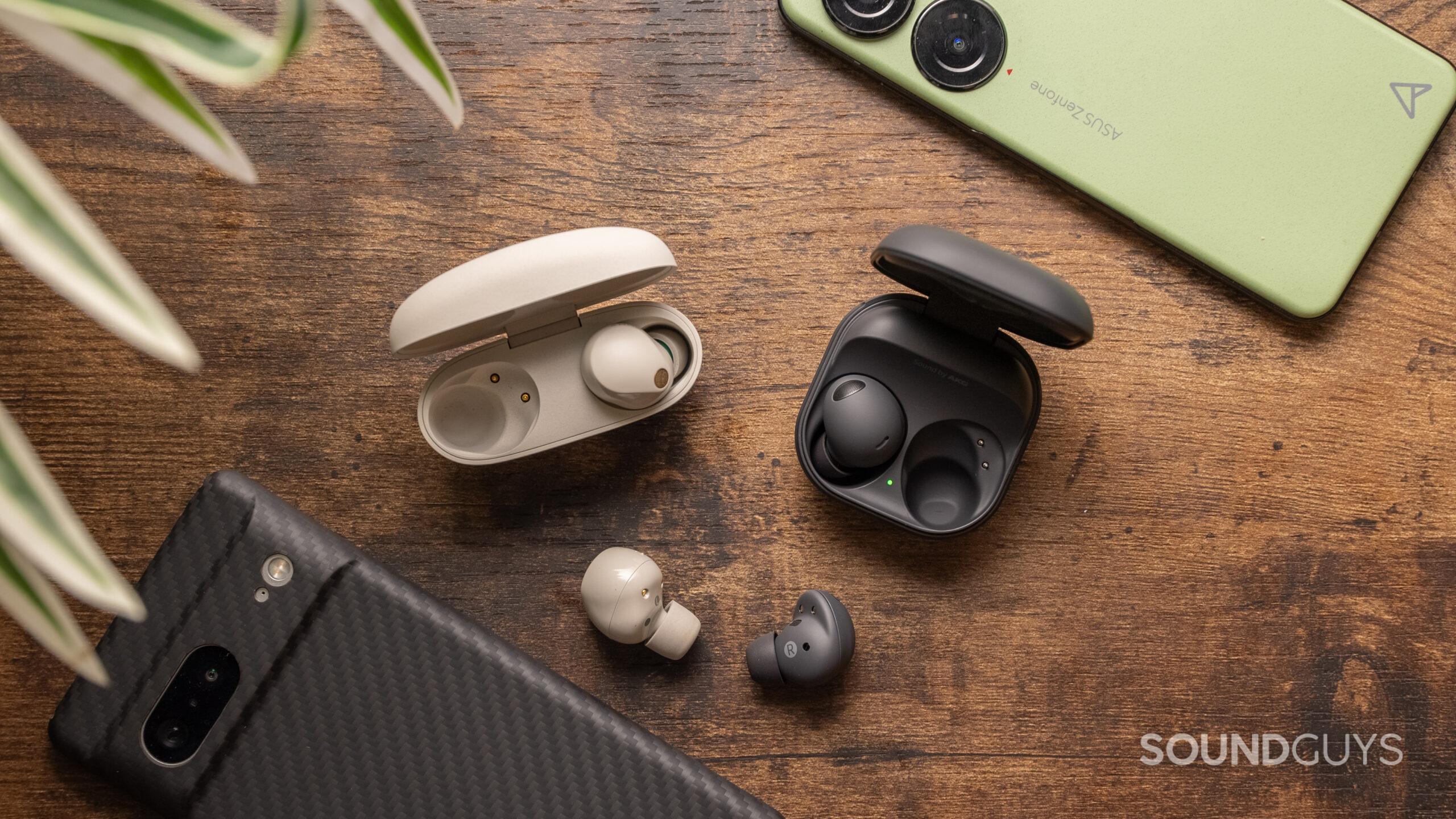 The Sony WF-1000XM5 and Samsung Galaxy Buds 2 Pro rest on a wood surface with one bud of each outside of the case.