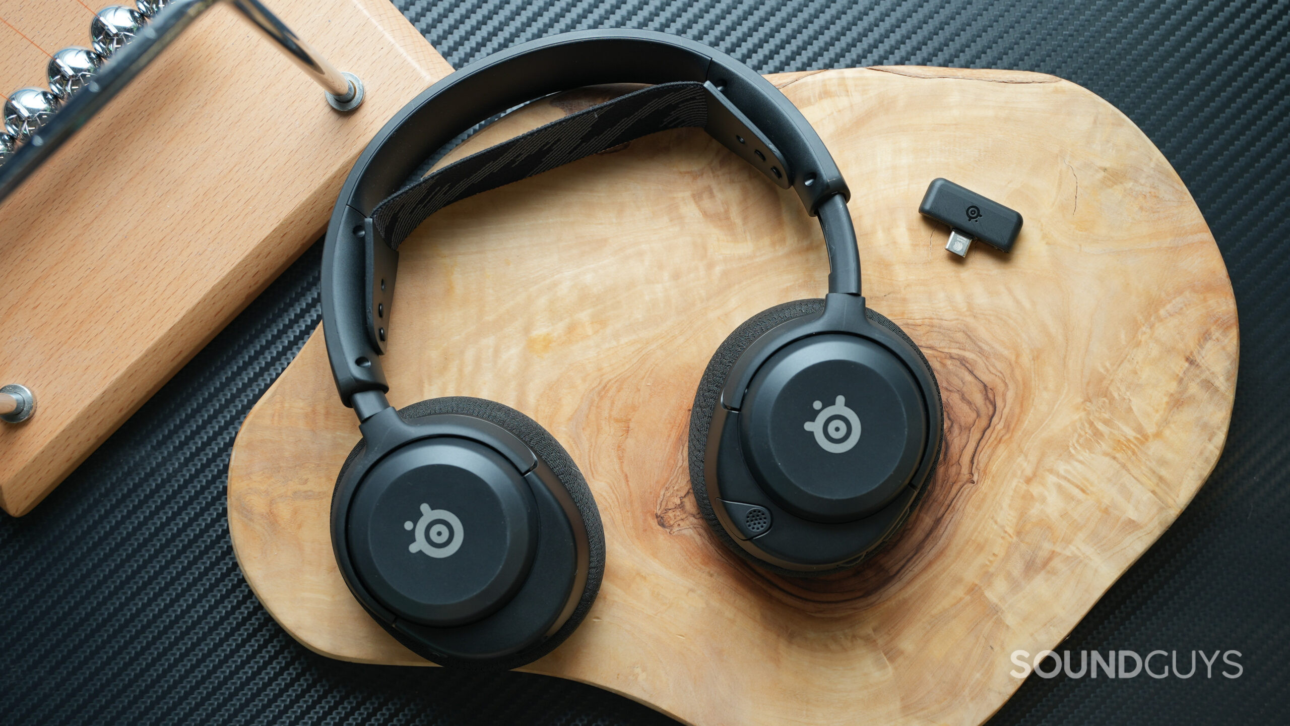 The SteelSeries Arctis Nova 4 sitting on a wooden table with its USB-C adapter next to it.