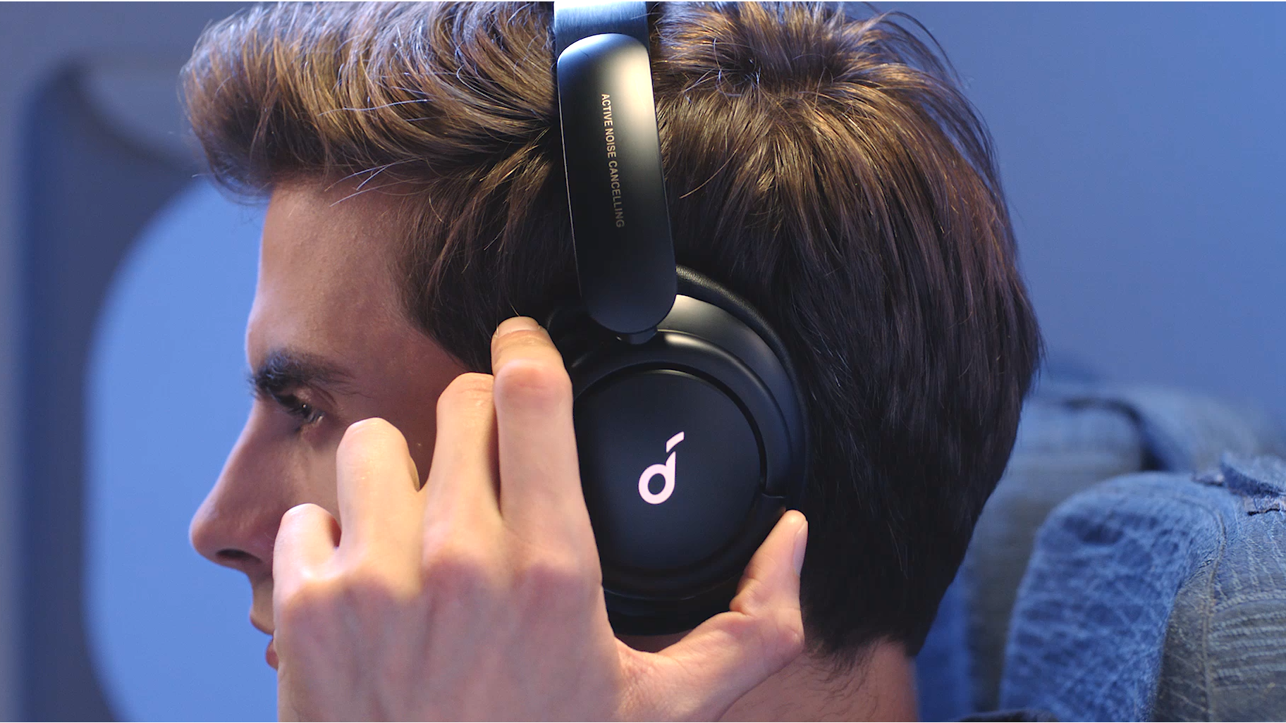 a man wearing a pair of headphones, holding the left earcup.