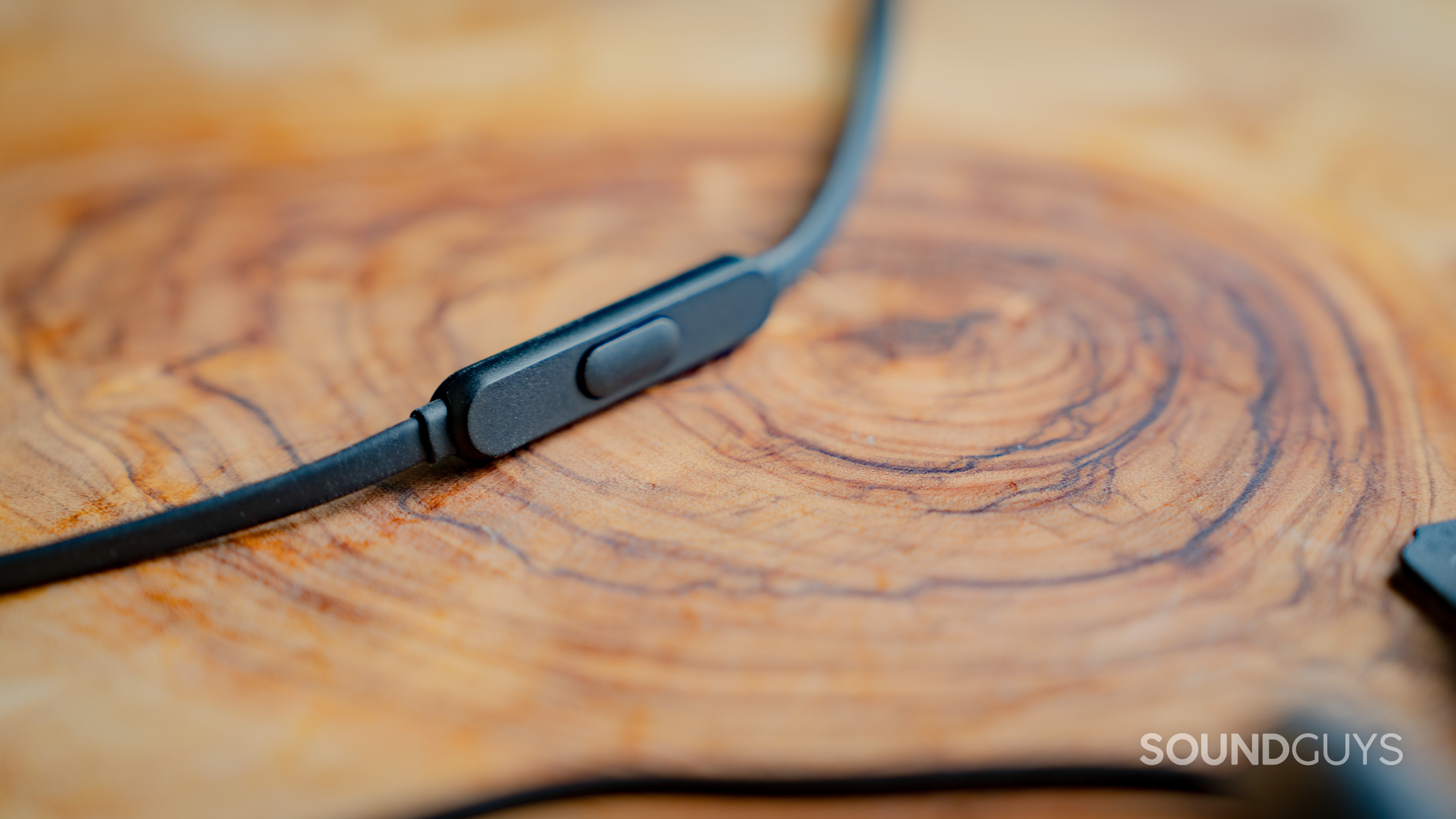 A closeup of the HyperX Cloud Earbuds II inline microphone and multifunction button against the backdrop of a wooden table.