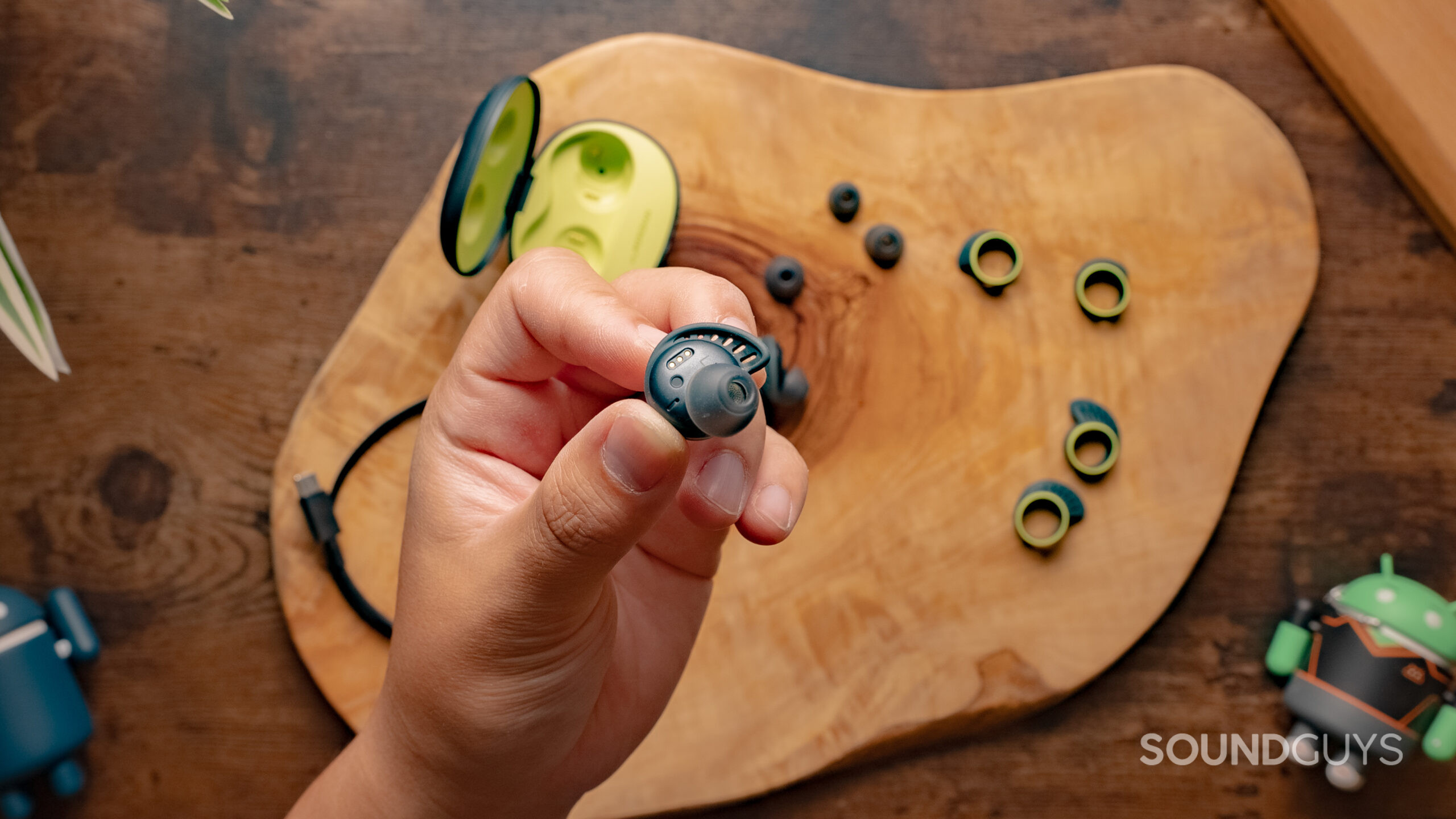 A hand holds one of the LG TONE Free fit TF7 earbuds above the case and accessories in the background.