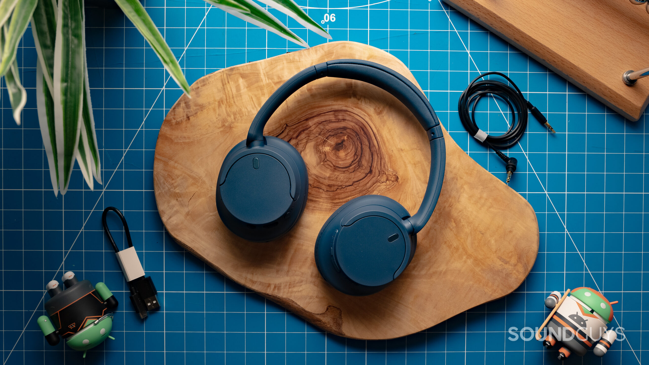 The Sony WH-CH720N with the ear cups rotated flat, showing the exterior plastic housing, resting on a wood surface with a grid in the background.