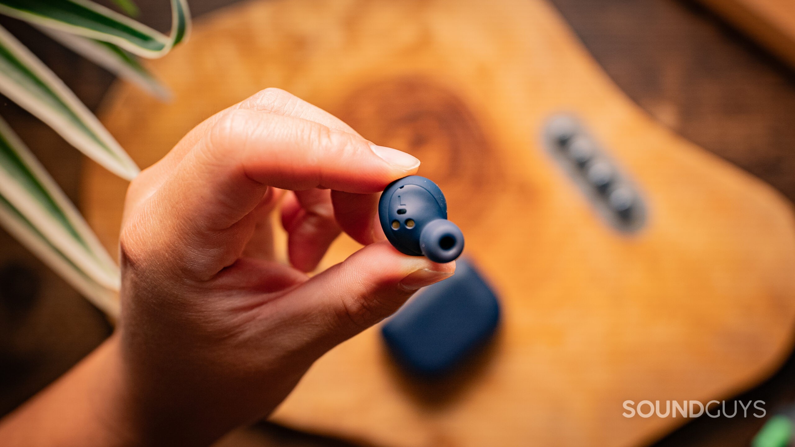 A hand holds the Jabra Elite 8 Active earbud, showing the shape, with the case in the background.