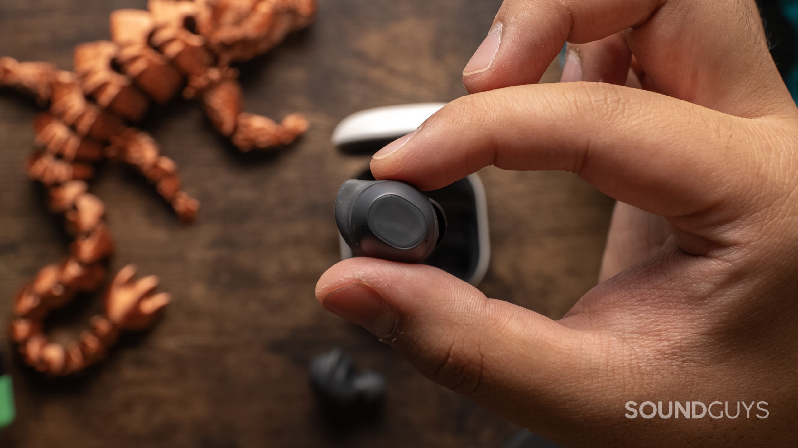 The Samsung Galaxy Buds FE, as held in front of a table top.
