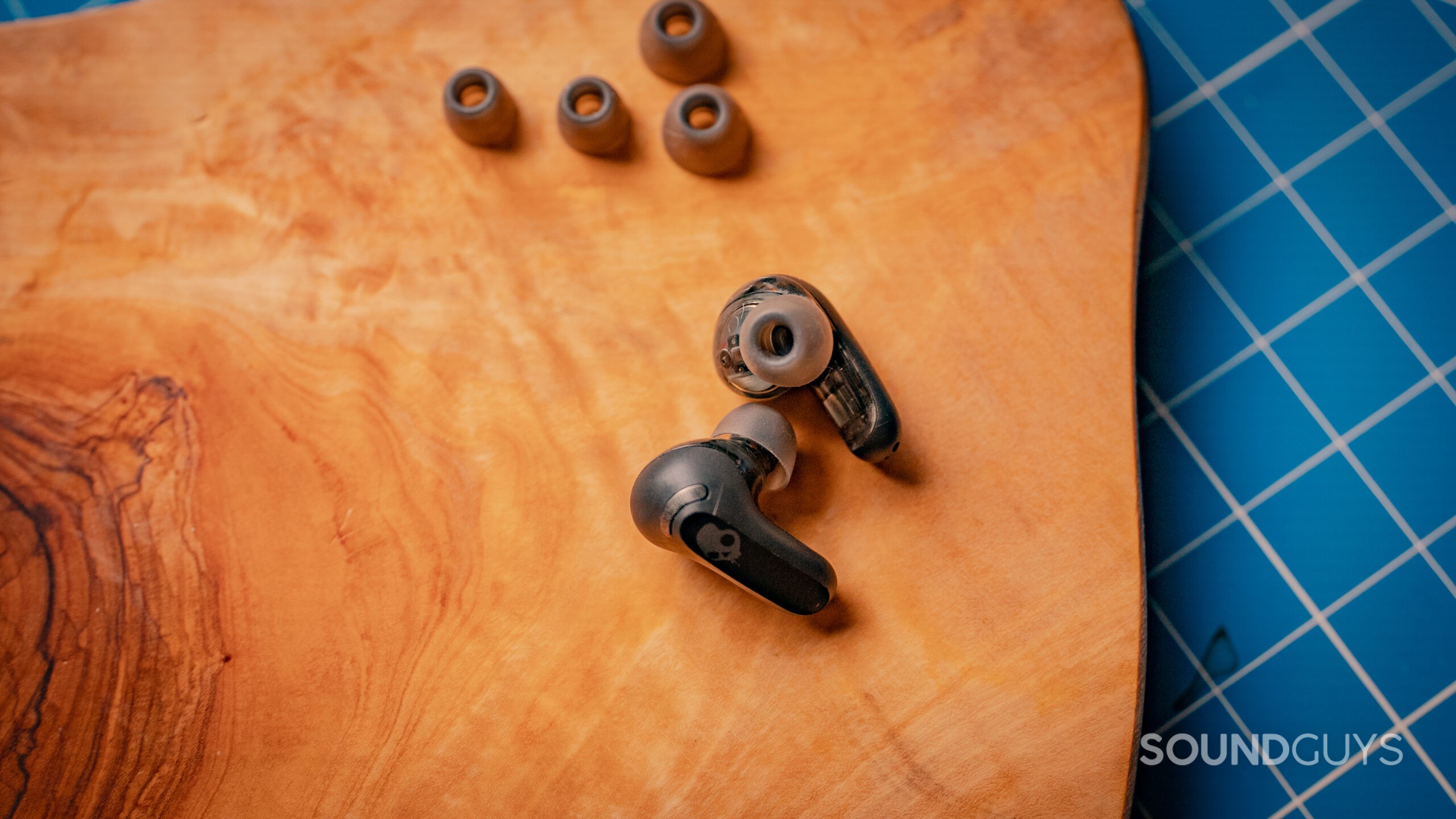 A close up the Skullcandy Rail ANC buds on a wood surface with accompanying spare ear tips.