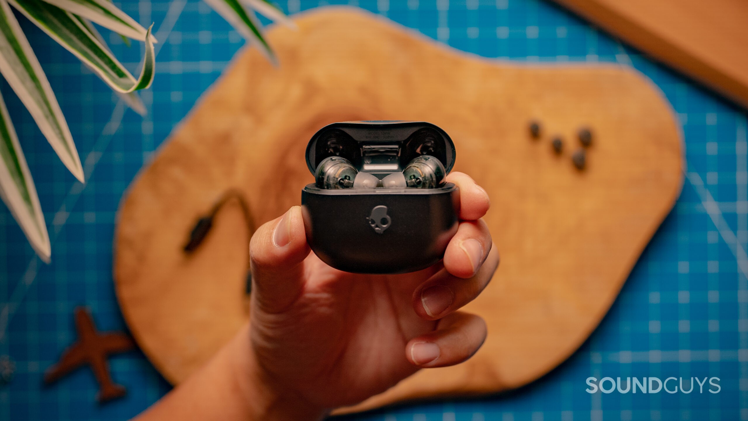 A hand holds the open case of the Skullcandy Rail ANC above a wood surface.