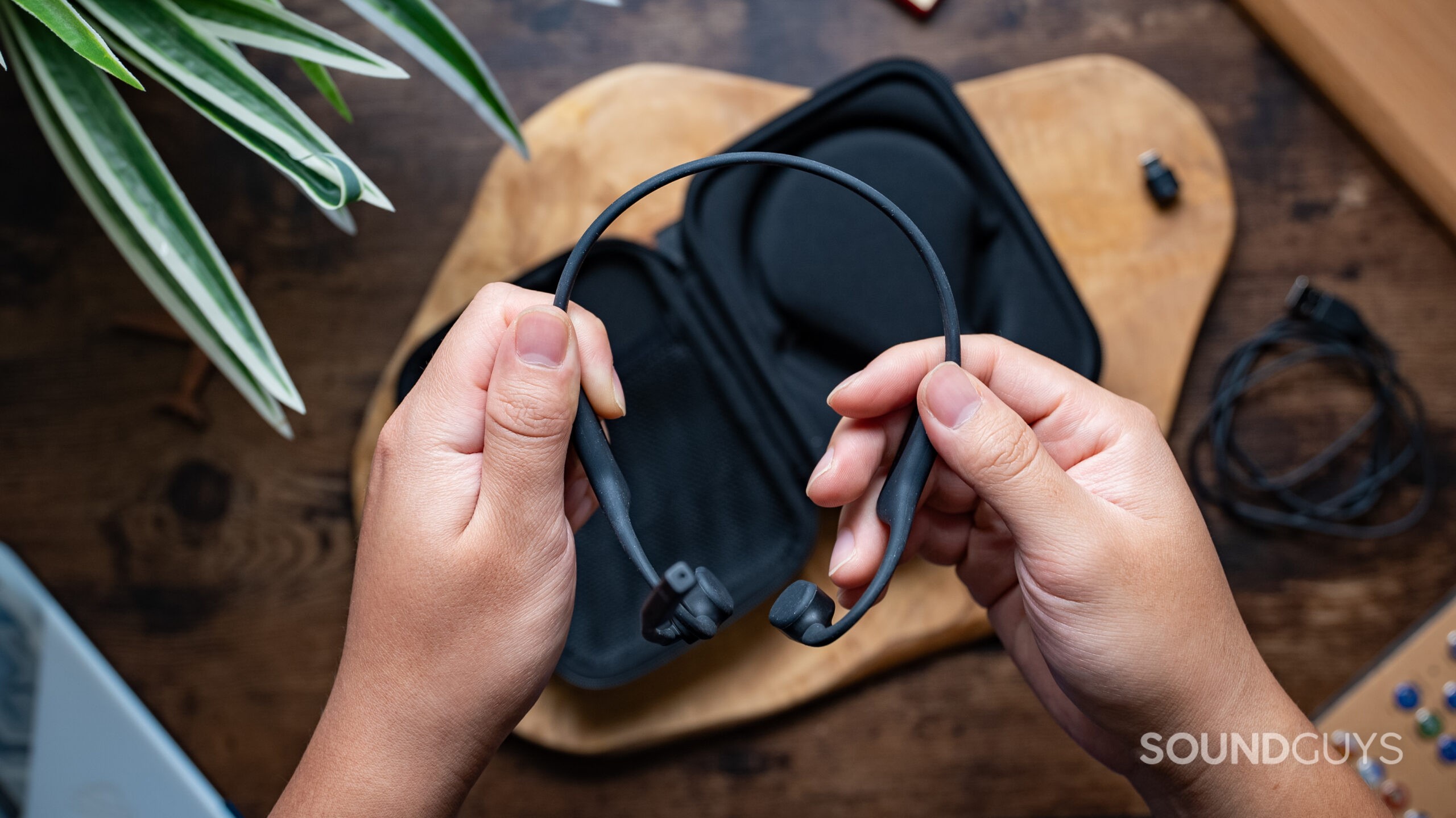 Two hands hold the Shokz OpenComm 2 UC with the case in the background.