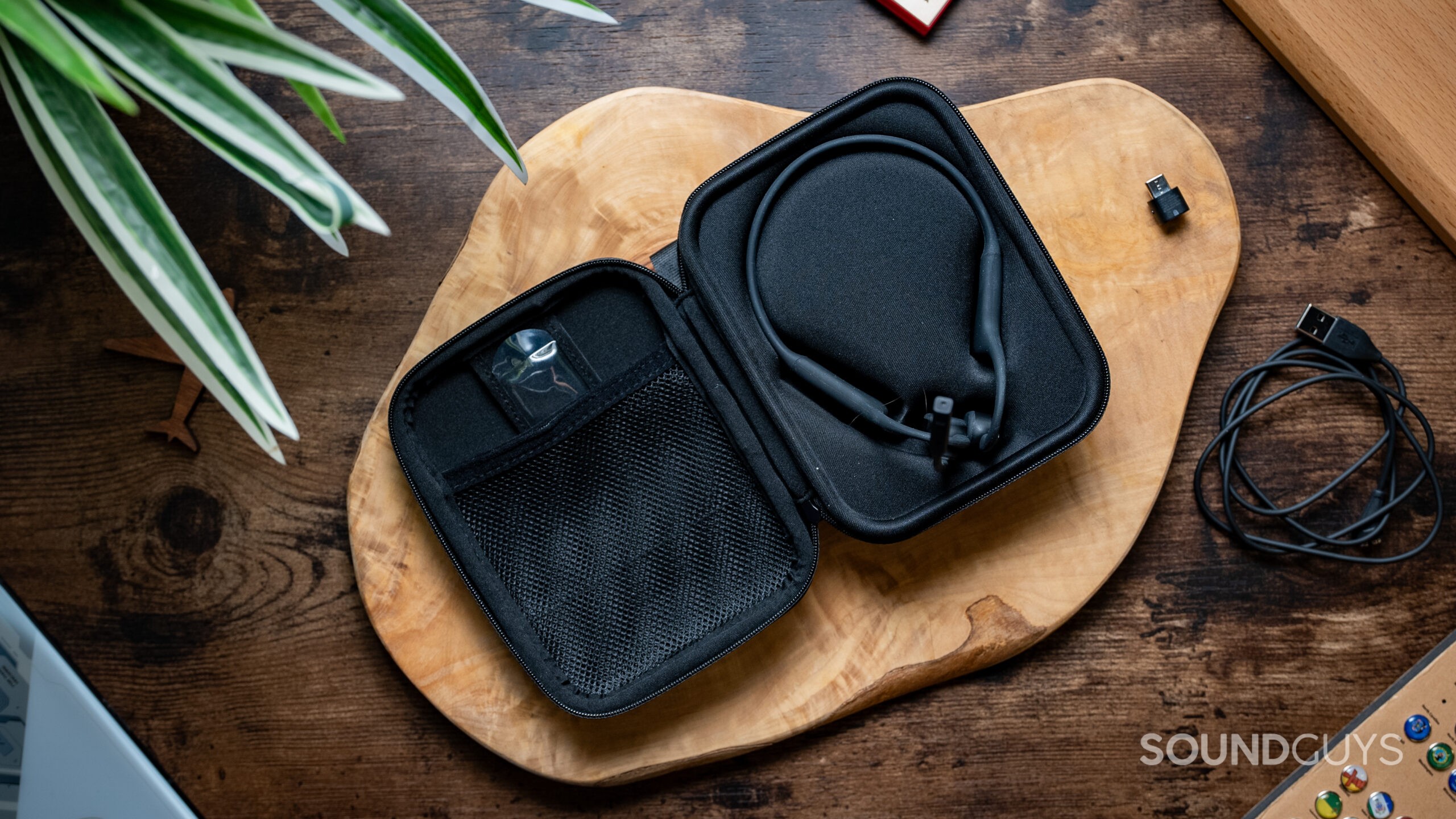 The zip case for the Shokz OpenComm2 UC rests on a wood table unzipped showing the headset inside.
