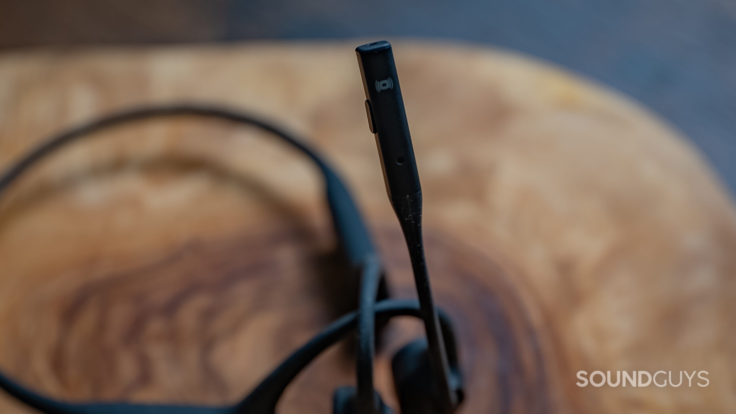 A close up of the Shokz OpenComm2 UC showing the boom microphone on a wood surface.