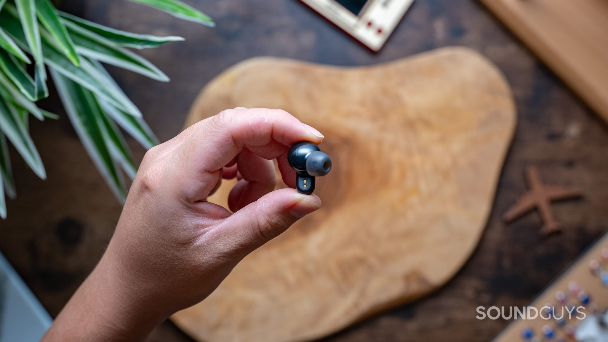 The Skullcandy Dime 3 earbuds held in a hand above a table. 