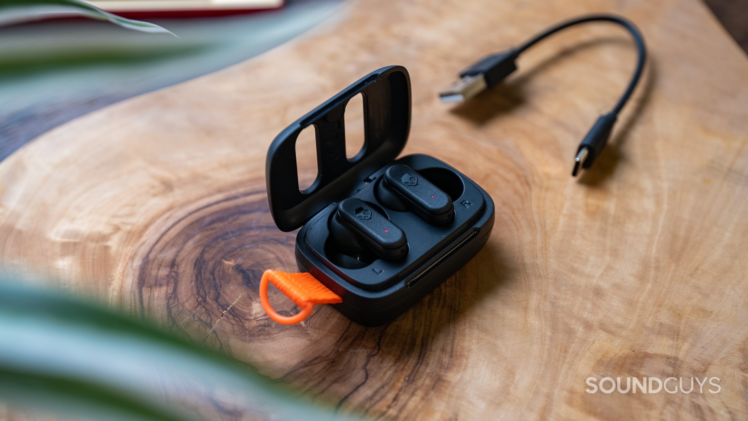 Skullcandy Dime 3 earbuds in their charging case on a table next to the charging cable.