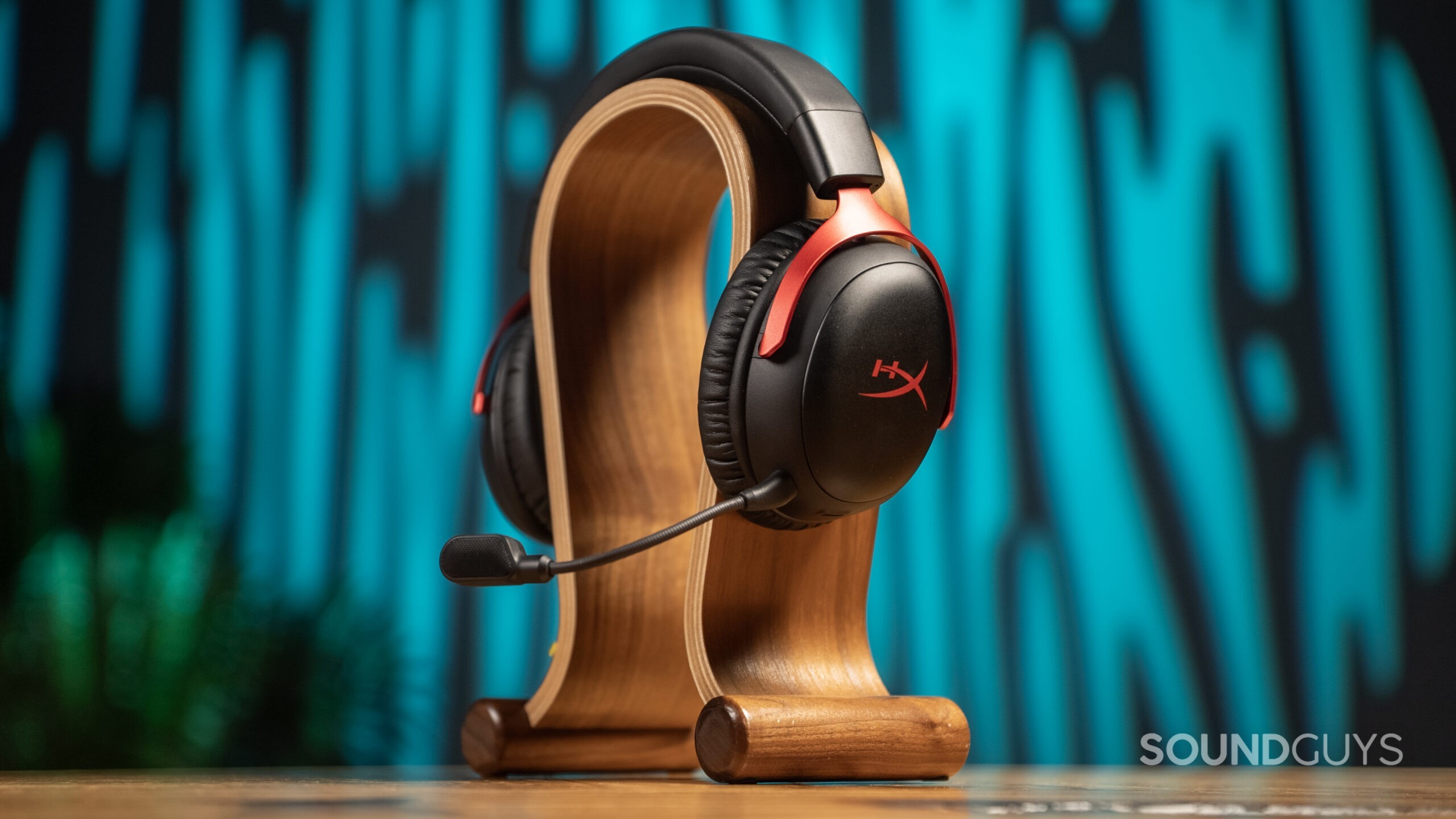The HyperX Cloud III Wireless sits atop a wooden omega-shaped headphone stand.