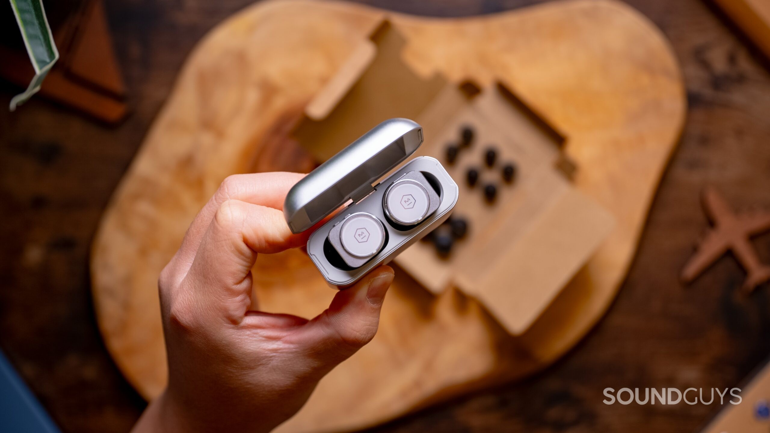 Master &amp; Dynamic MW09 earbuds in charging case held above a table.