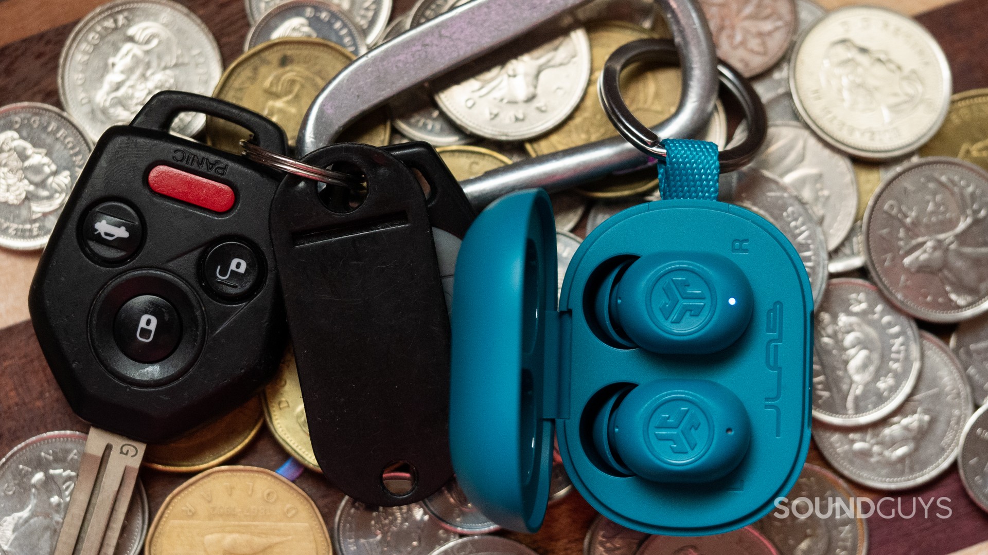 A photo of the Jlab JBuds Mini attached to a keychain, atop coins.