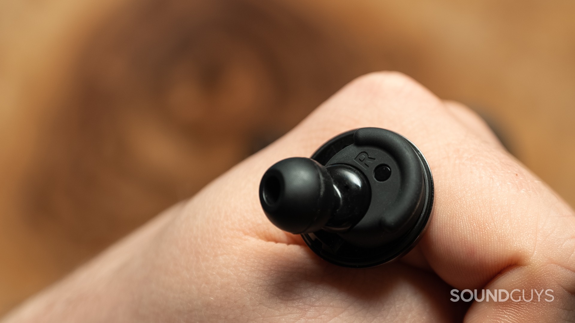 A photo of the Denon PerL Pro on someone's hand, with ear sensor visible.