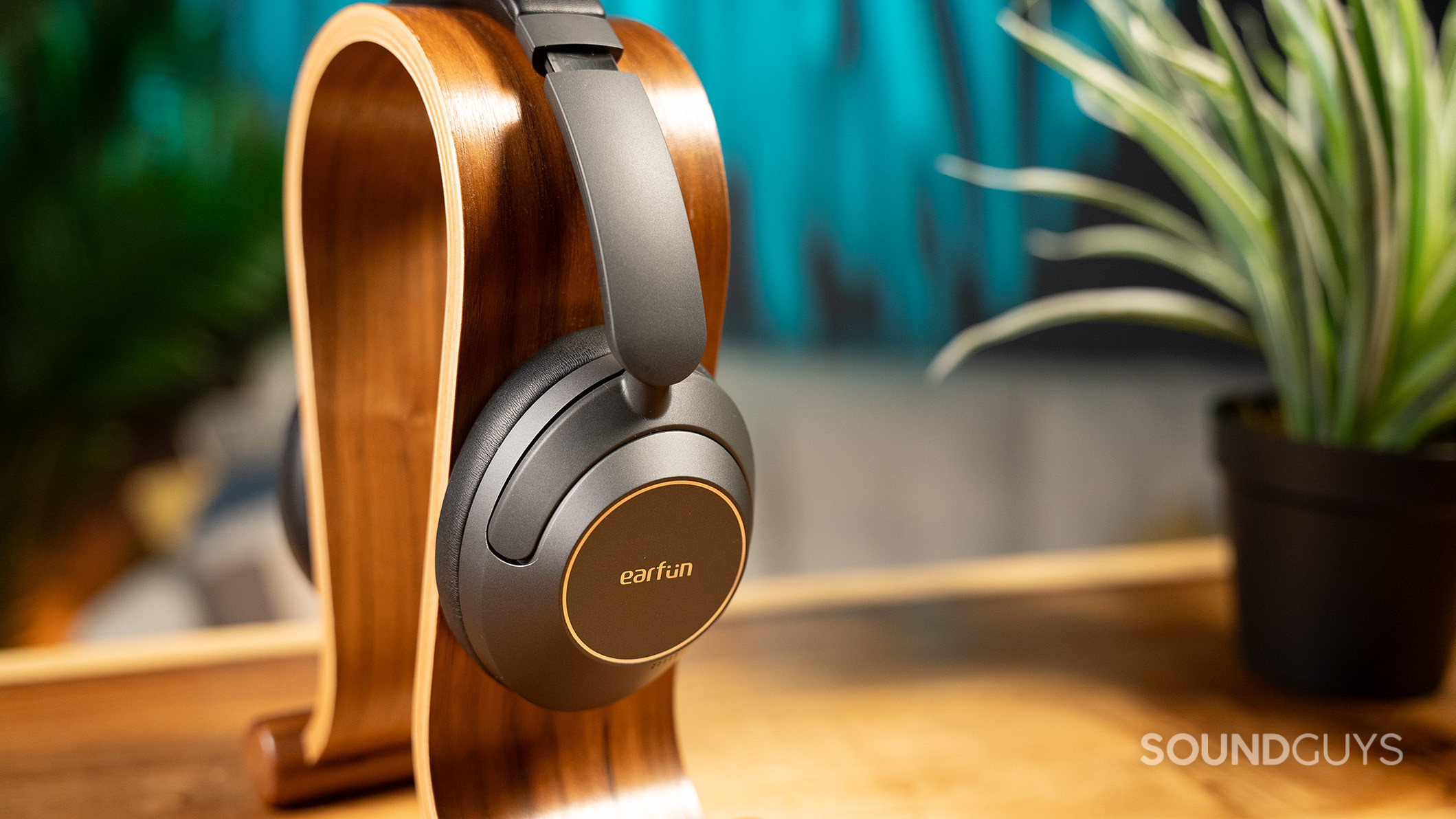 EarFun Wave Pro headphones on a wood stand next to a plant. 