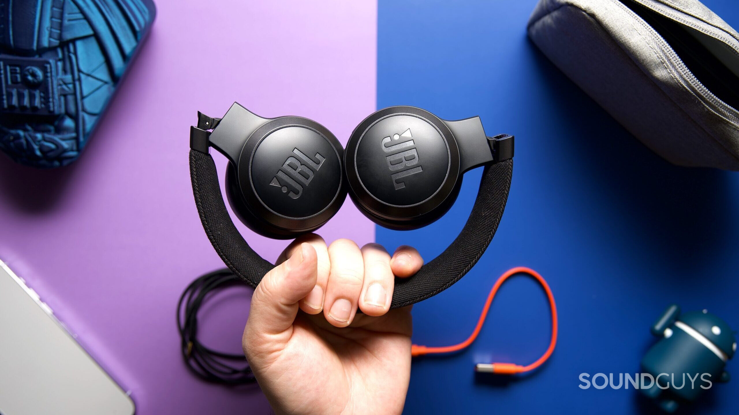 A hand holding a folded up pair of JBL Live 670NC headphones