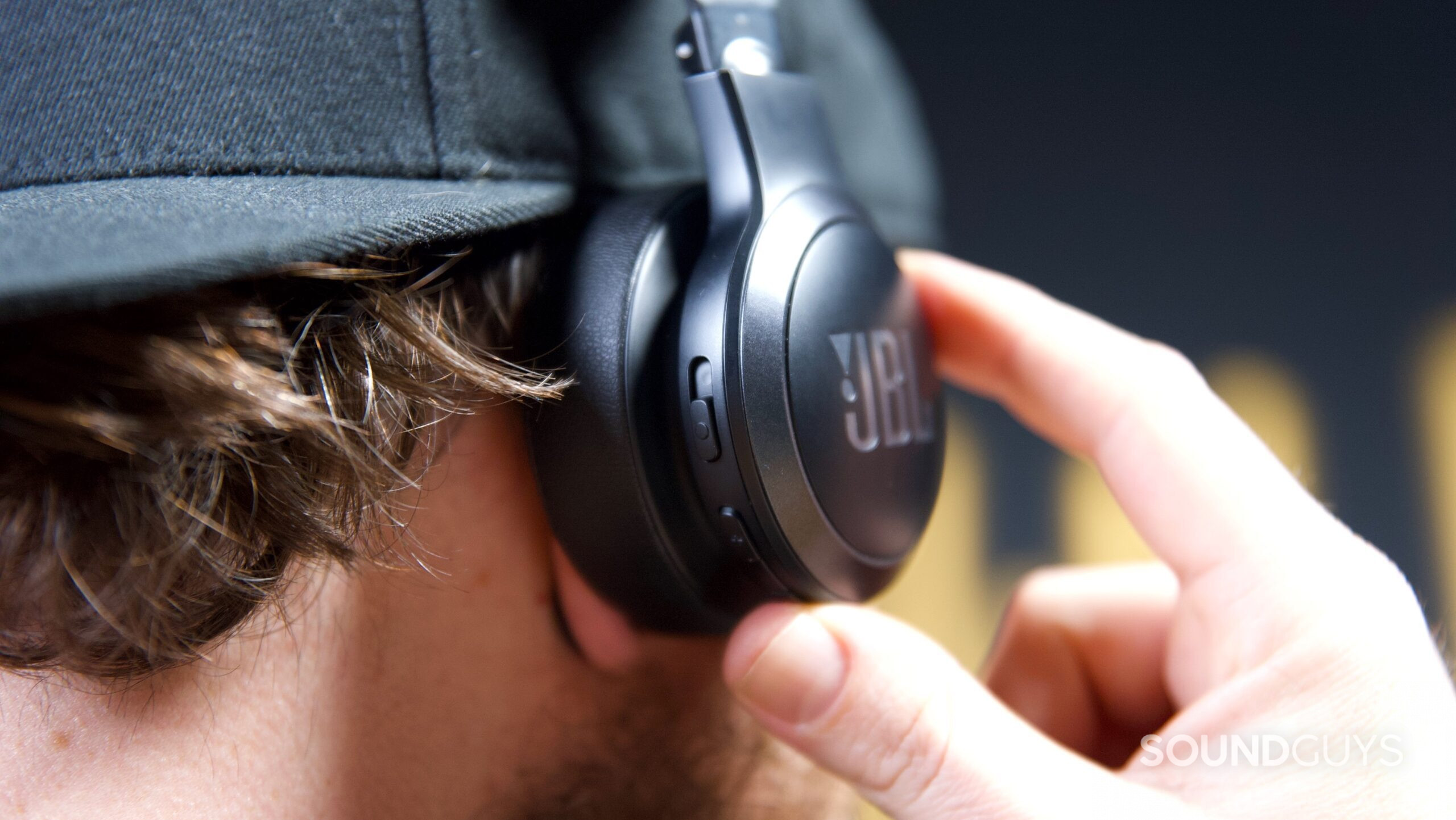 A man pressing the control buttons on a pair of JBL Live 670NC headphones