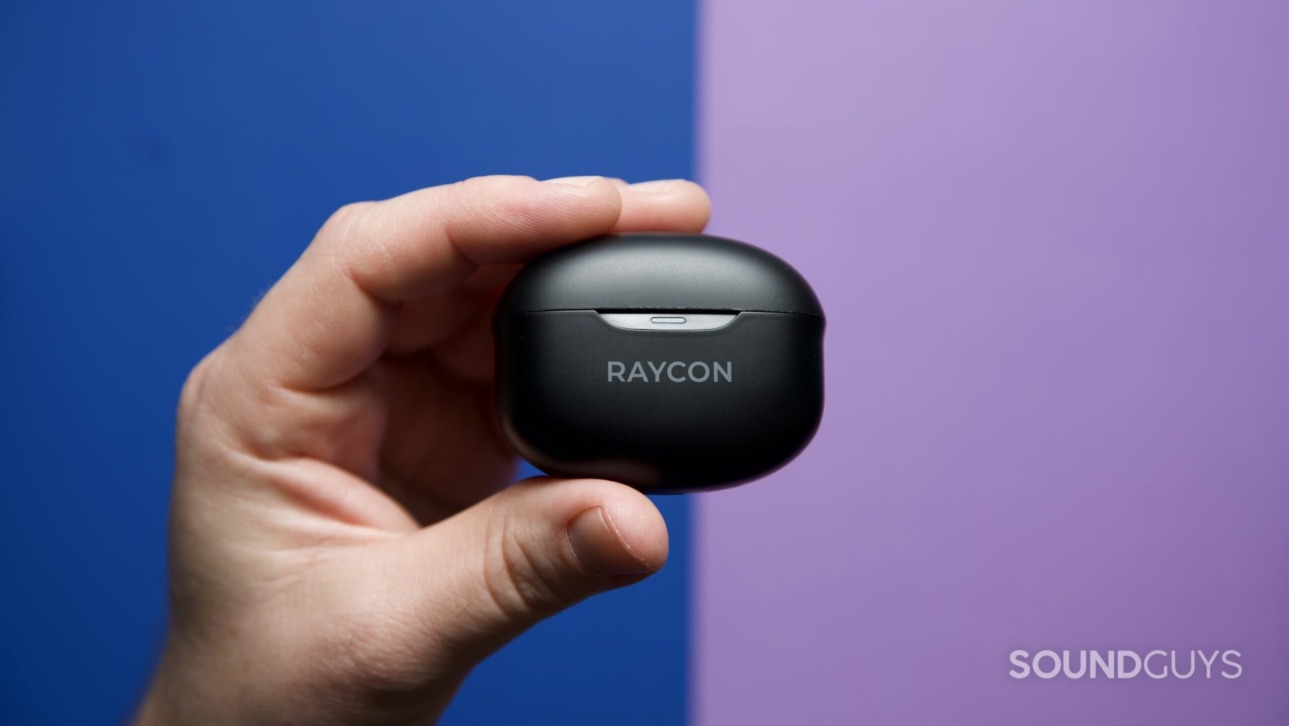 A hand holding a closed Raycon Everyday Earbuds charging case.