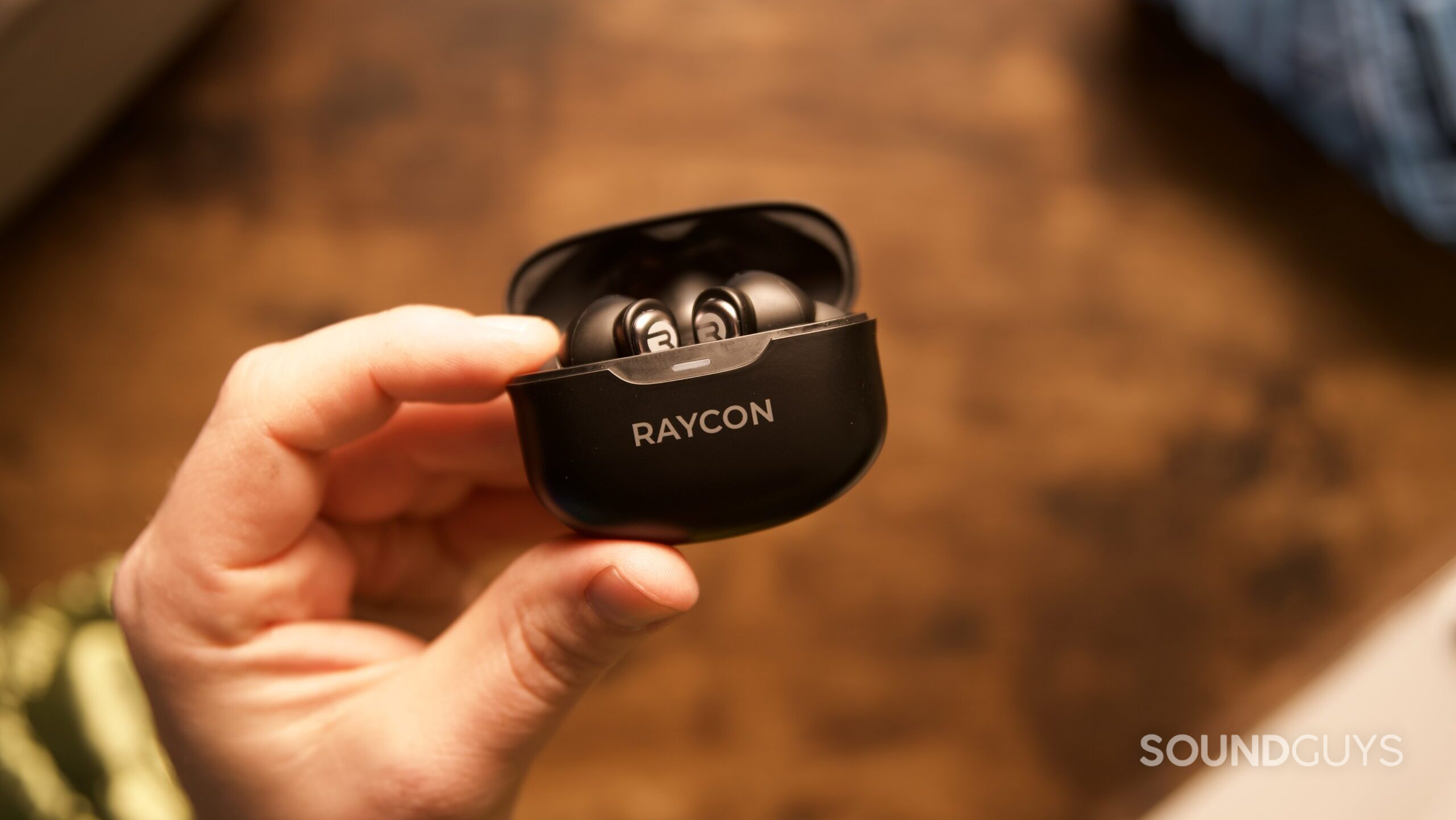 A hand holding an open Raycon Everday Earbuds Pro charging case with earbuds inside