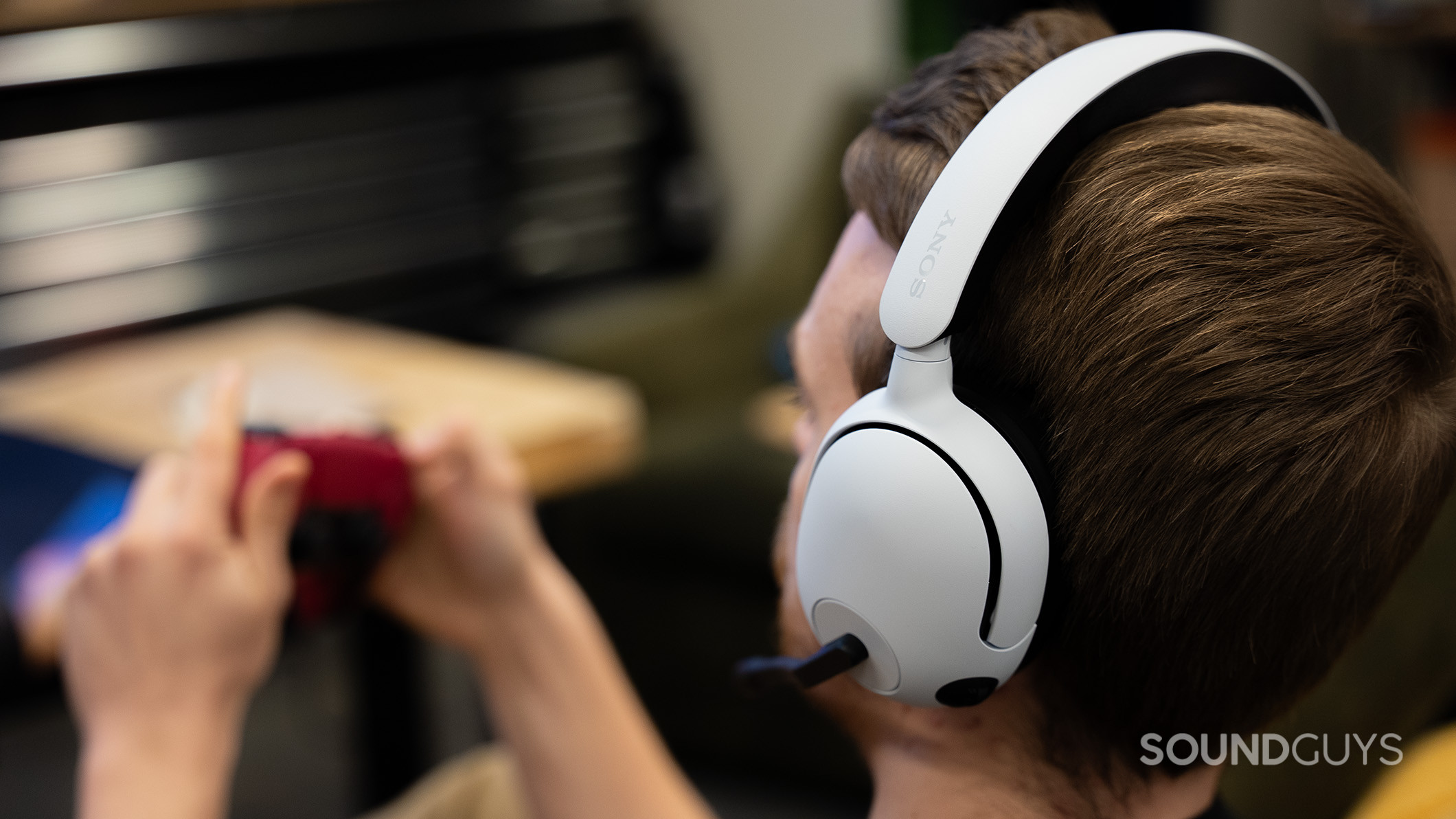 A man holding a PS5 controller while wearing the Sony INZONE H5 headphones. 