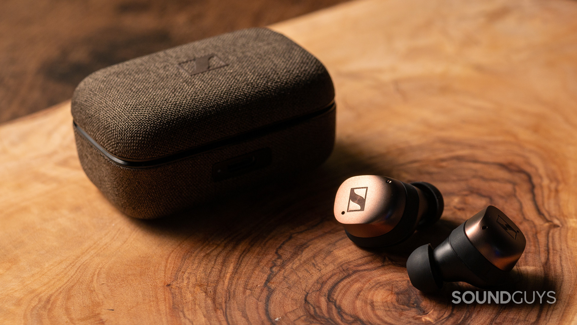 A photo of the Sennheiser MOMENTUM True Wireless 4 on a wooden table, outside of their charging case.