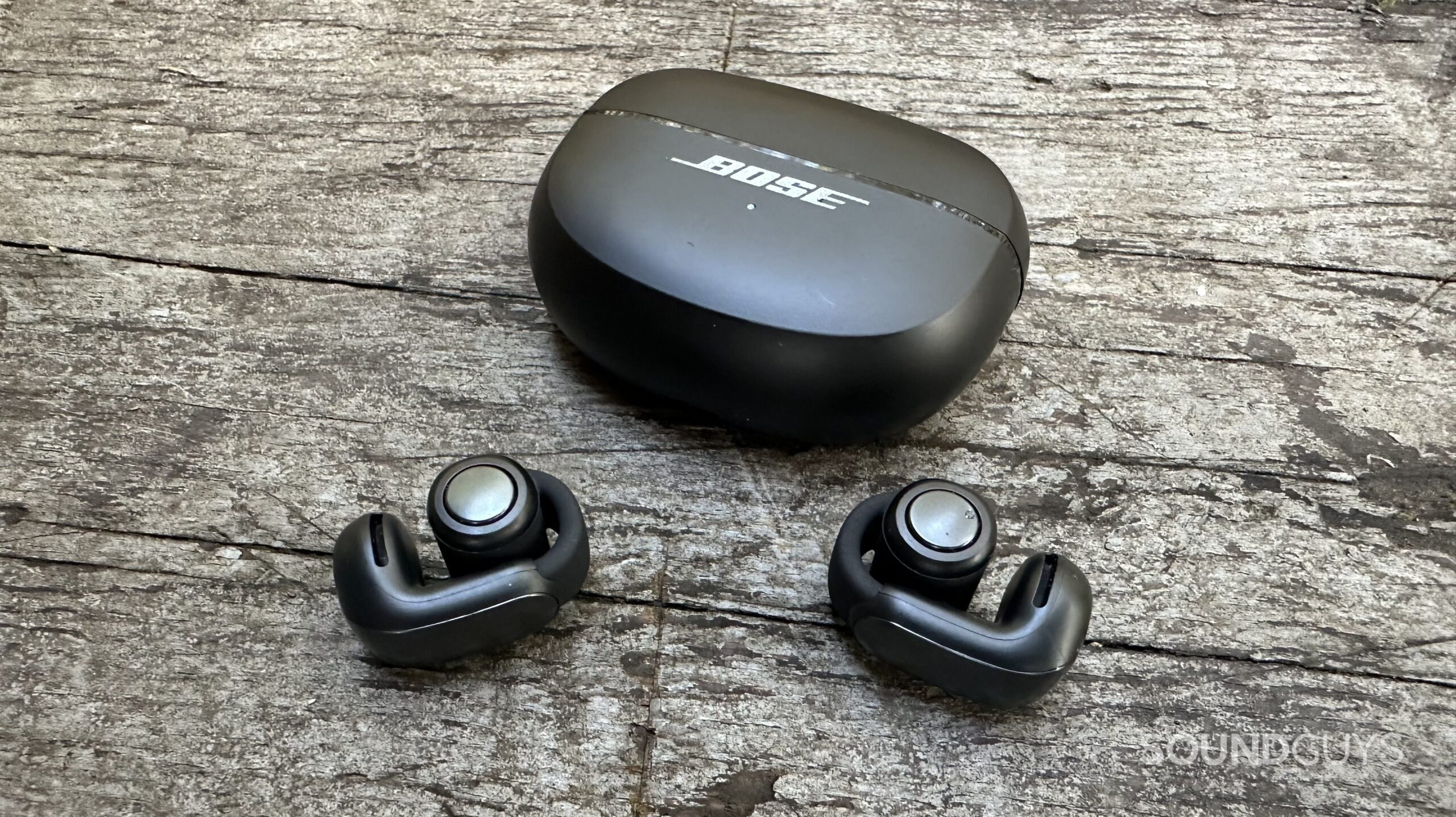 Bose Ultimate Open Earbuds and their charging case on a grey bench
