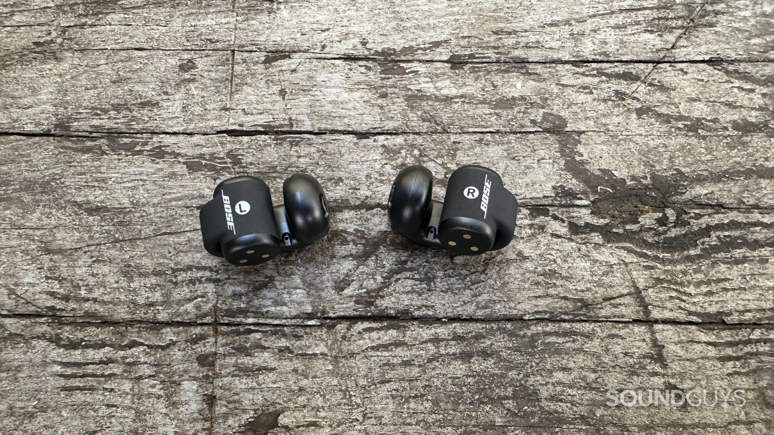 Close up shot of the Bose Ultra Open Earbuds from behind while on a grey bench