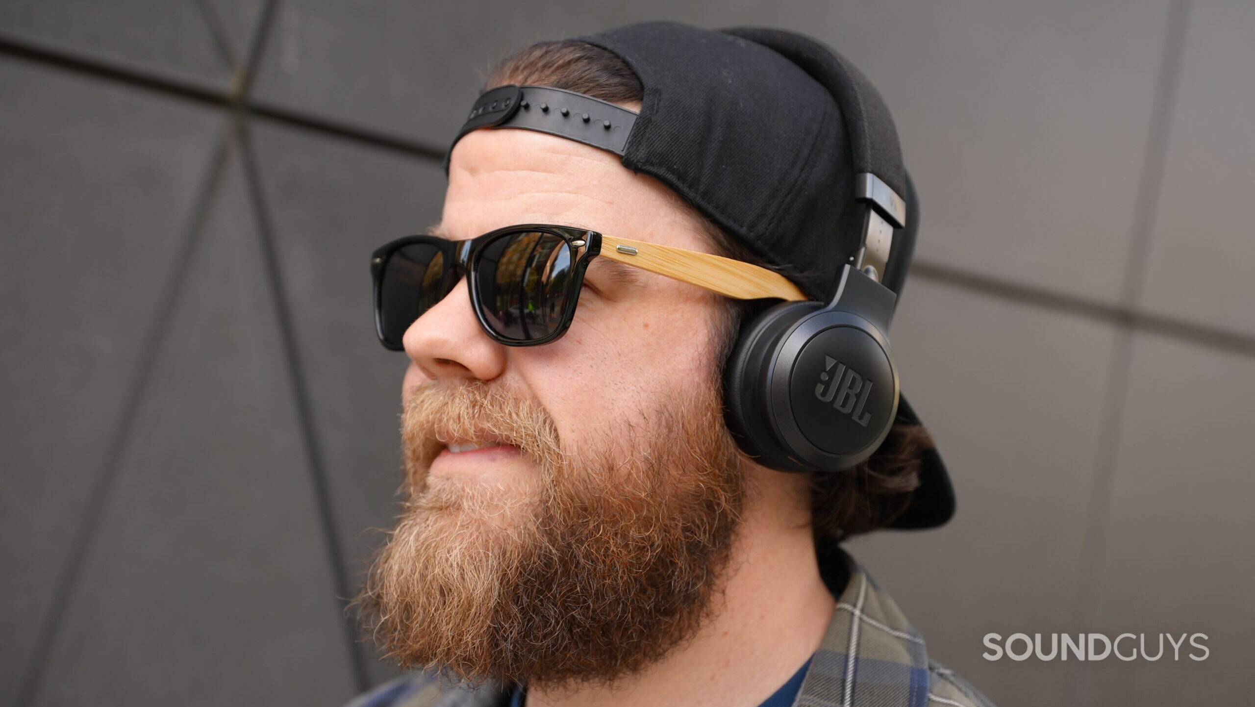 A man wearing the JBL Livew 670NC headphones and sunglasses looking happy