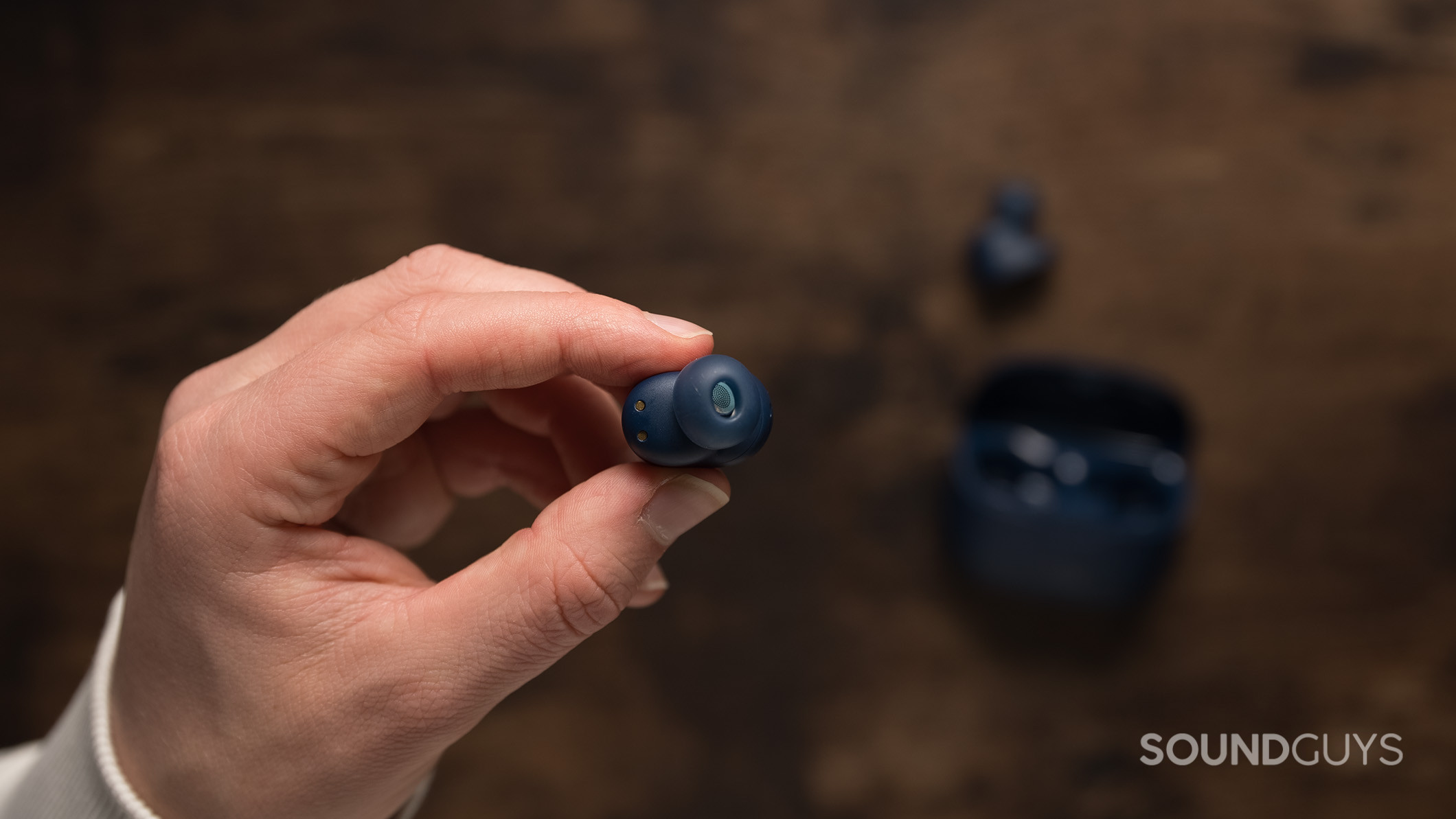 A hand holds a single JBL Tune Buds earbud over a table. 