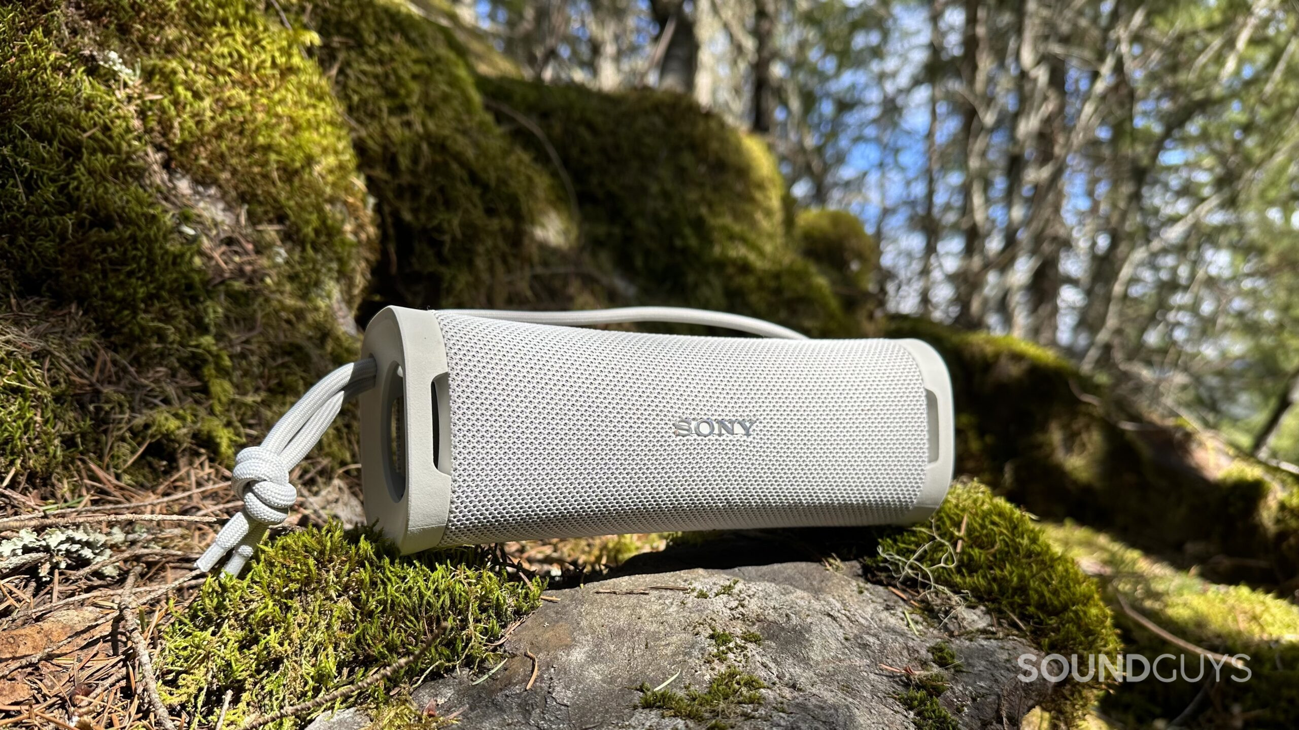 The Sony ULT Field 1 speaker sitting on a mossy rock in the sunlight.