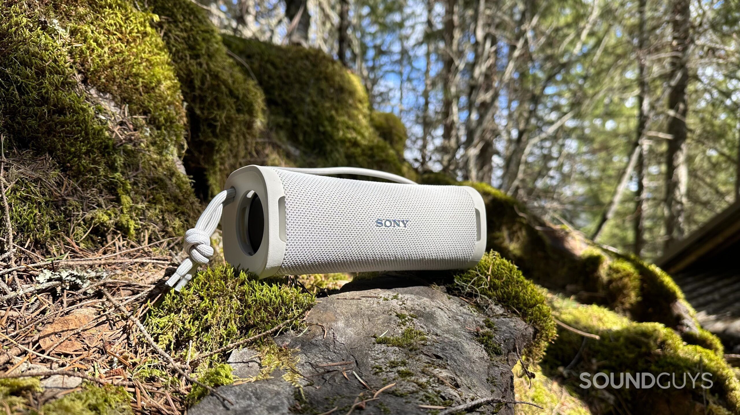 A Sony ULT Field 1 speaker placed on a mossy rock in the outdoors