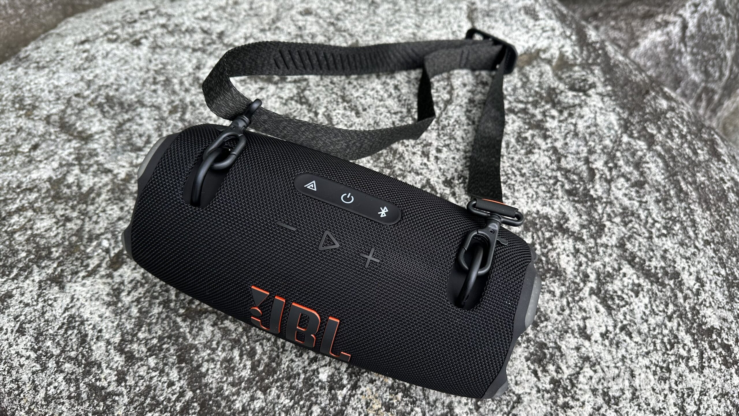 A JBL Xtreme 4 is placed on a rock in an outdoor setting.