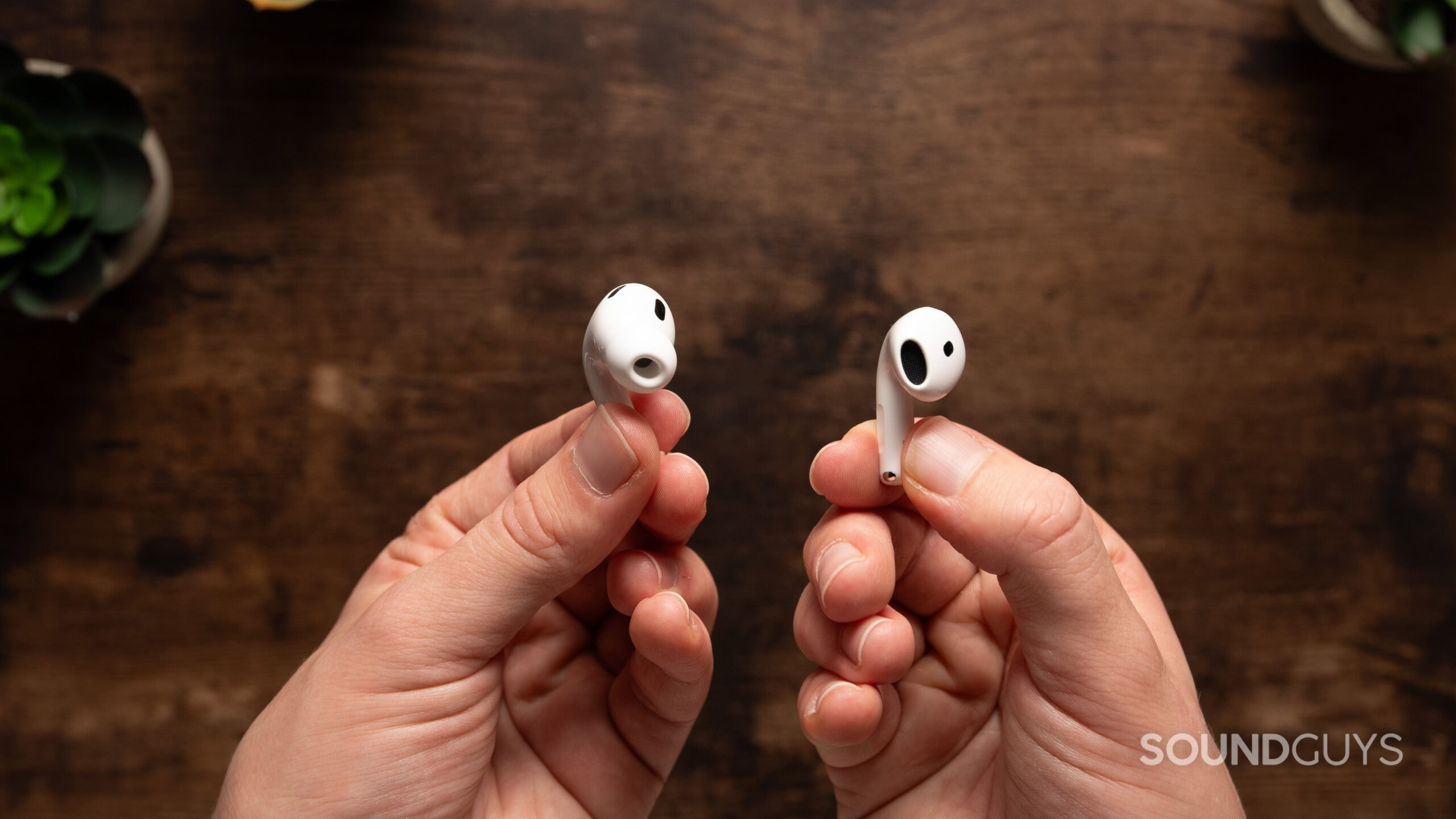 AirPods 4 vs AirPods Pro 2 earbud drivers One hand holds an AirPods 4 earbud without an ear tip while another hand holds an AirPods Pro 2 earbud with an ear tip.
