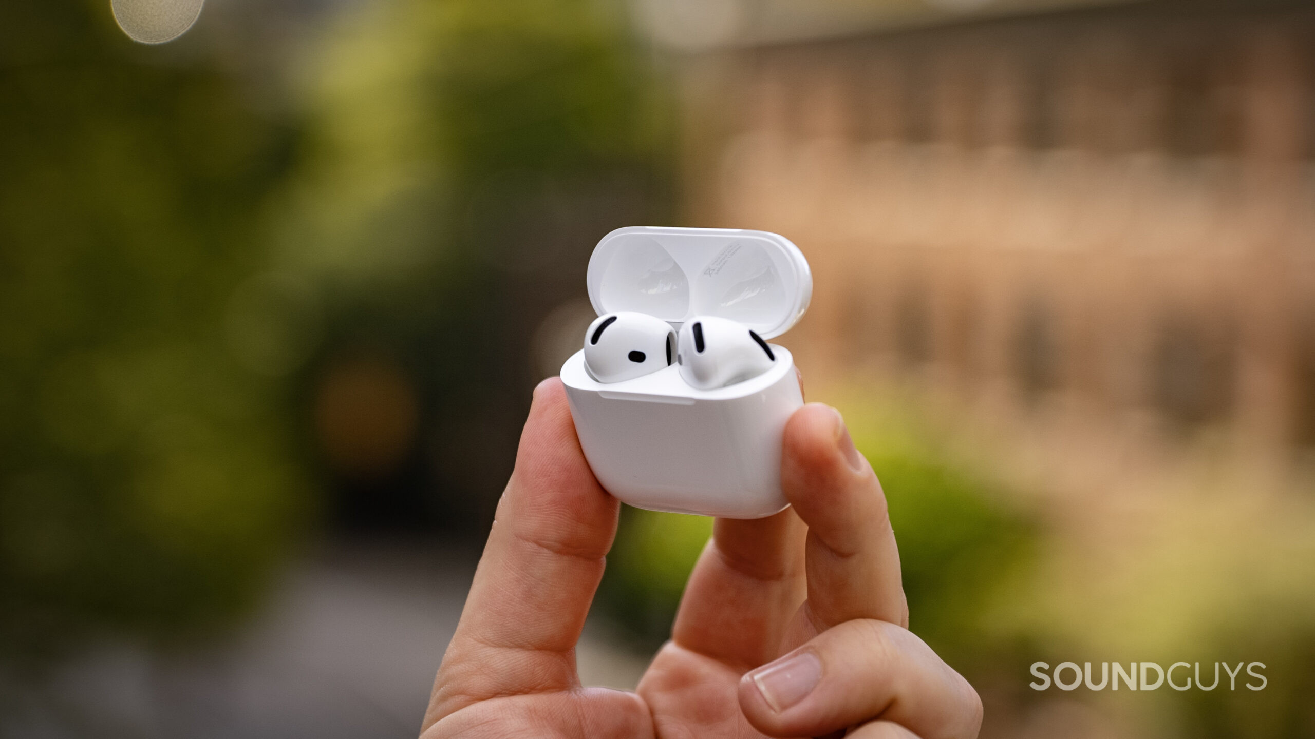 Apple AirPods 4 in hand outside front of building A hand holds the AirPods 4 earbuds inside their charging case.