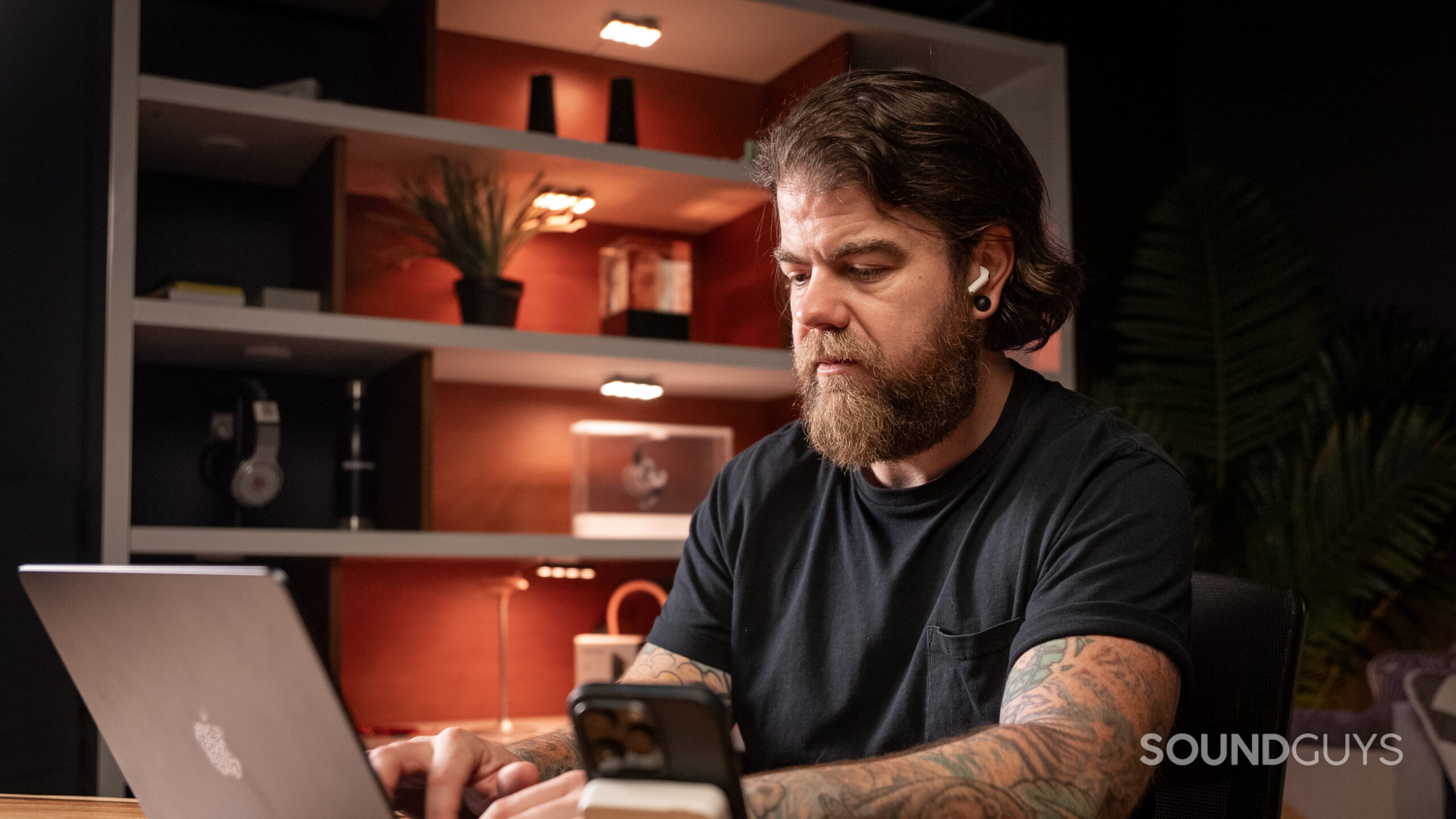 Apple AirPods 4 man wearing while working in studio A man at a desk looks at a computer while wearing AirPods 4.