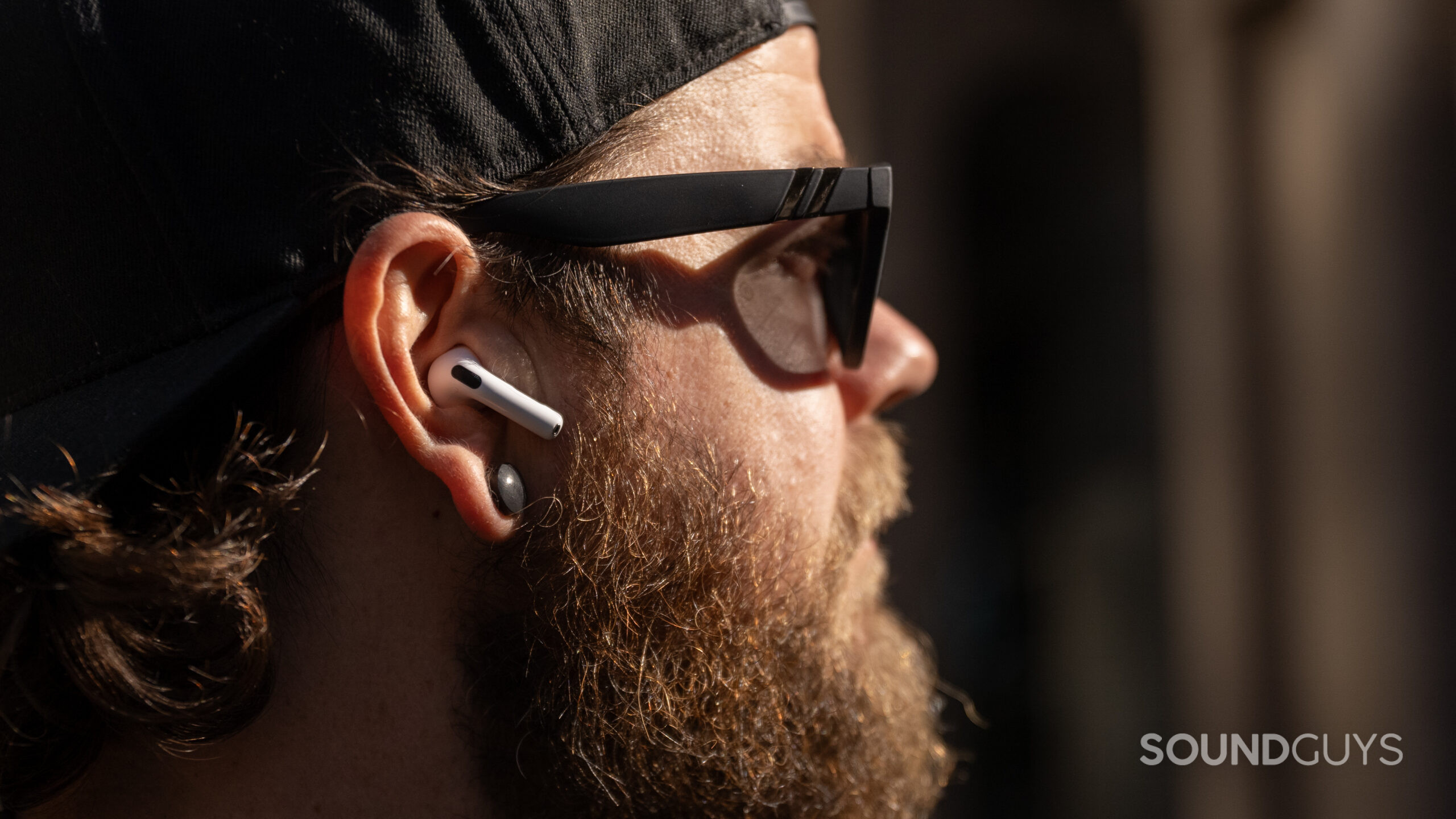 Apple AirPods 4 wear A close-up photo of a sunglasses-wearing man with beard and AirPods 4.