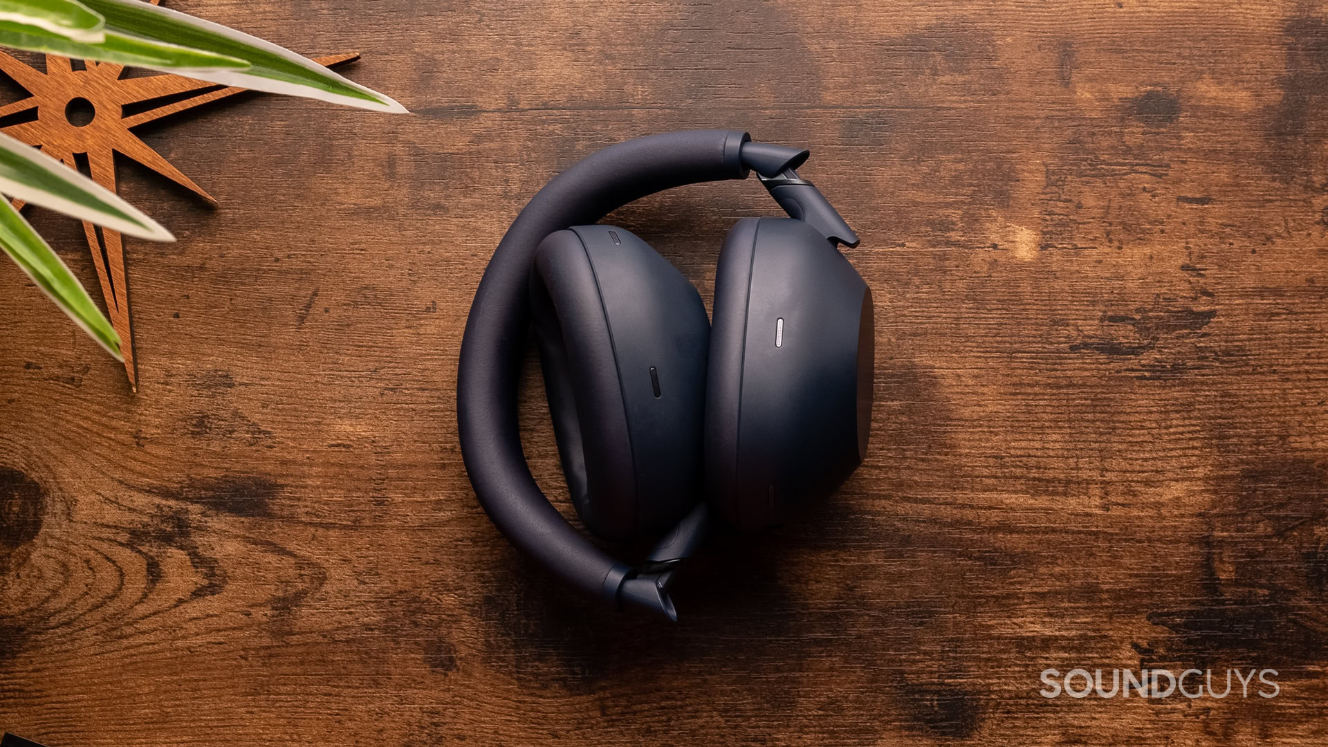 A photo of the Sony WH-1000XM6 folded up, sitting on a wooden desk.
