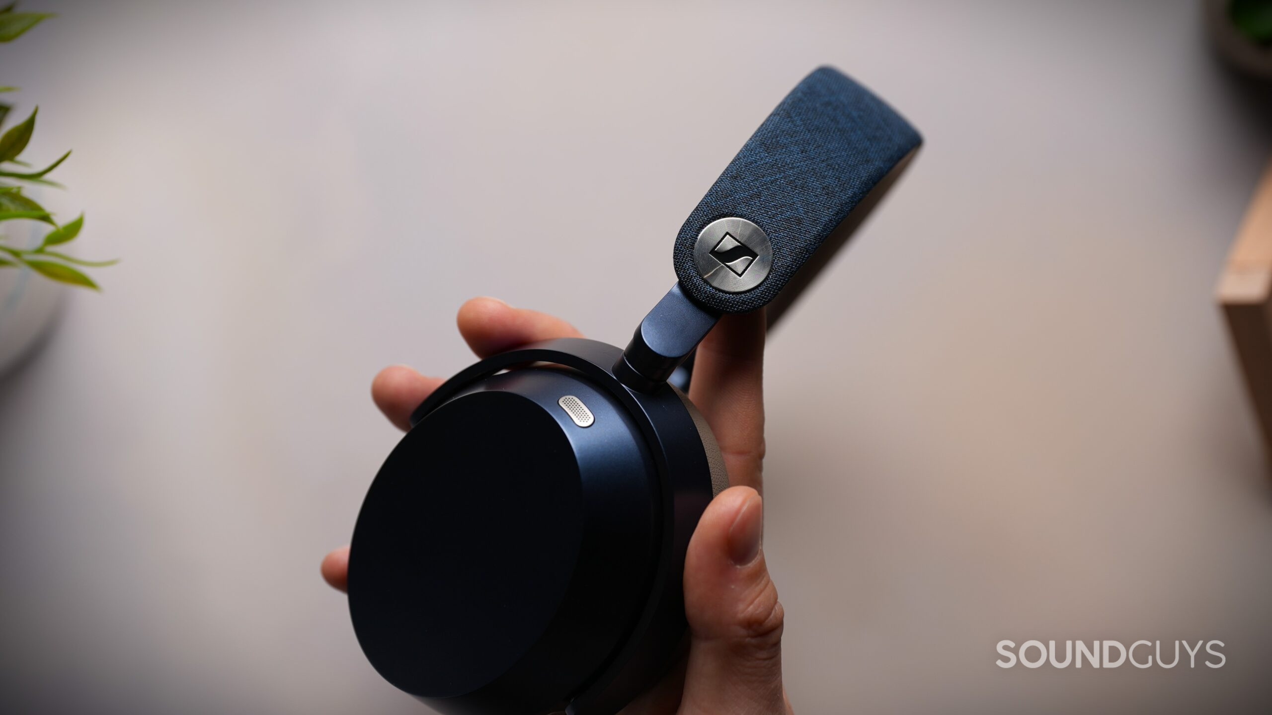 Close-up of the Sennheiser MOMENTUM 5 Wireless headband hinge and metallic Sennheiser logo detail while held in hand.